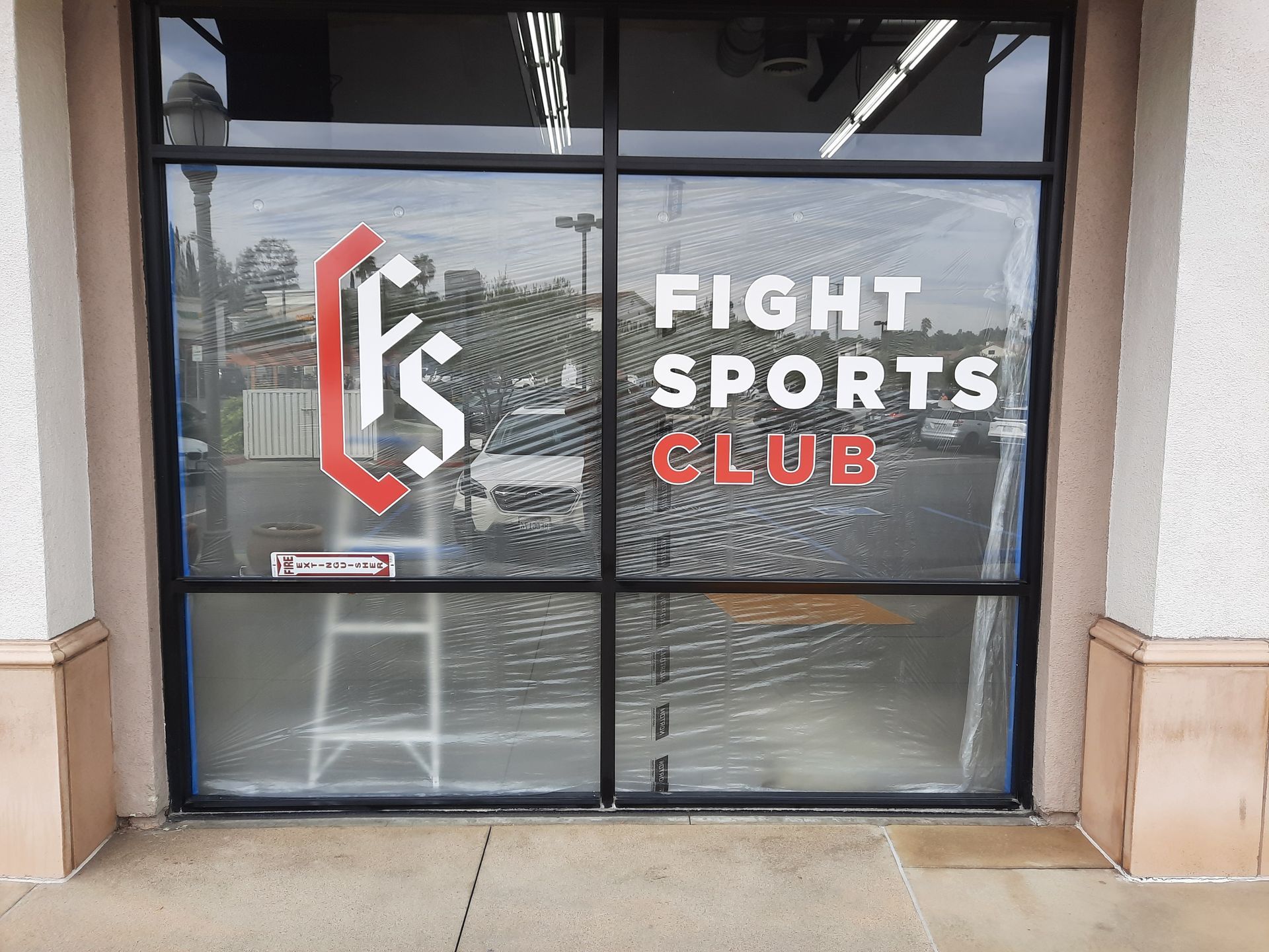 Storefront window for “Fight Sports Club” with black, white, and red signage.