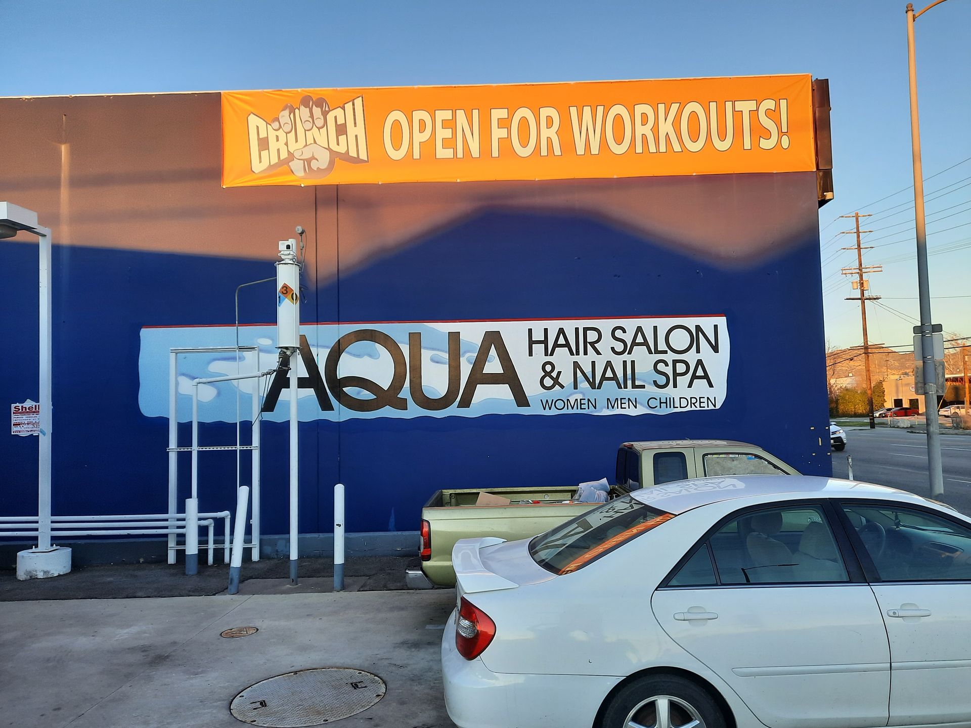 Aqua Hair Salon & Nail Spa storefront with orange “Open for workouts!” banner and parked white car