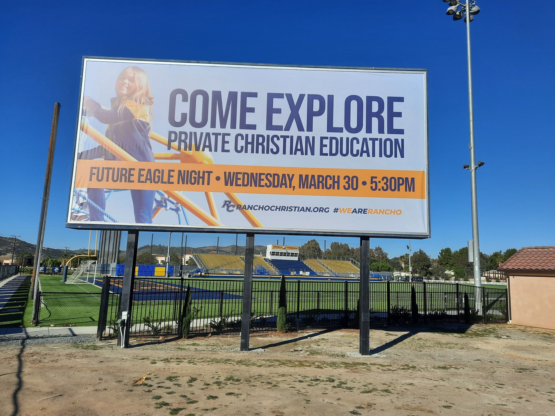 Billboard advertising private Christian education at Future Eagle Night, with blue sky and playground in background