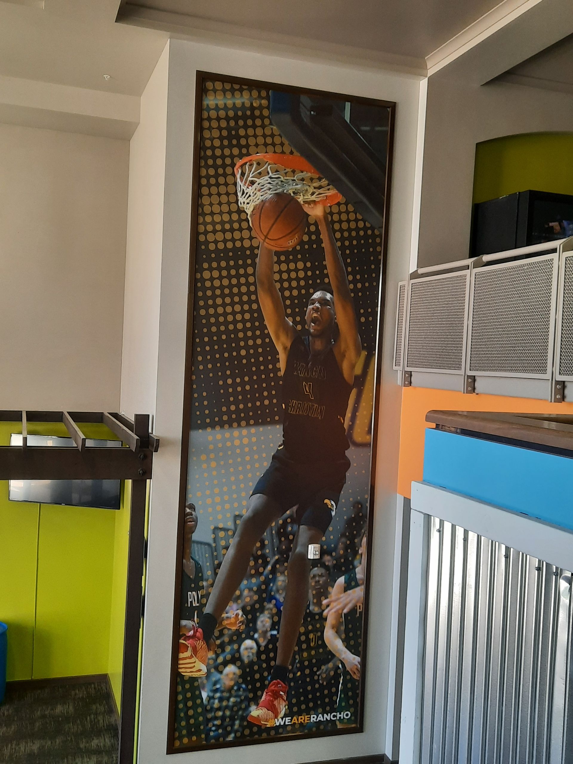 Vertical basketball mural showing a player dunking in orange and black, in a room with shelves and a lime cabinet.