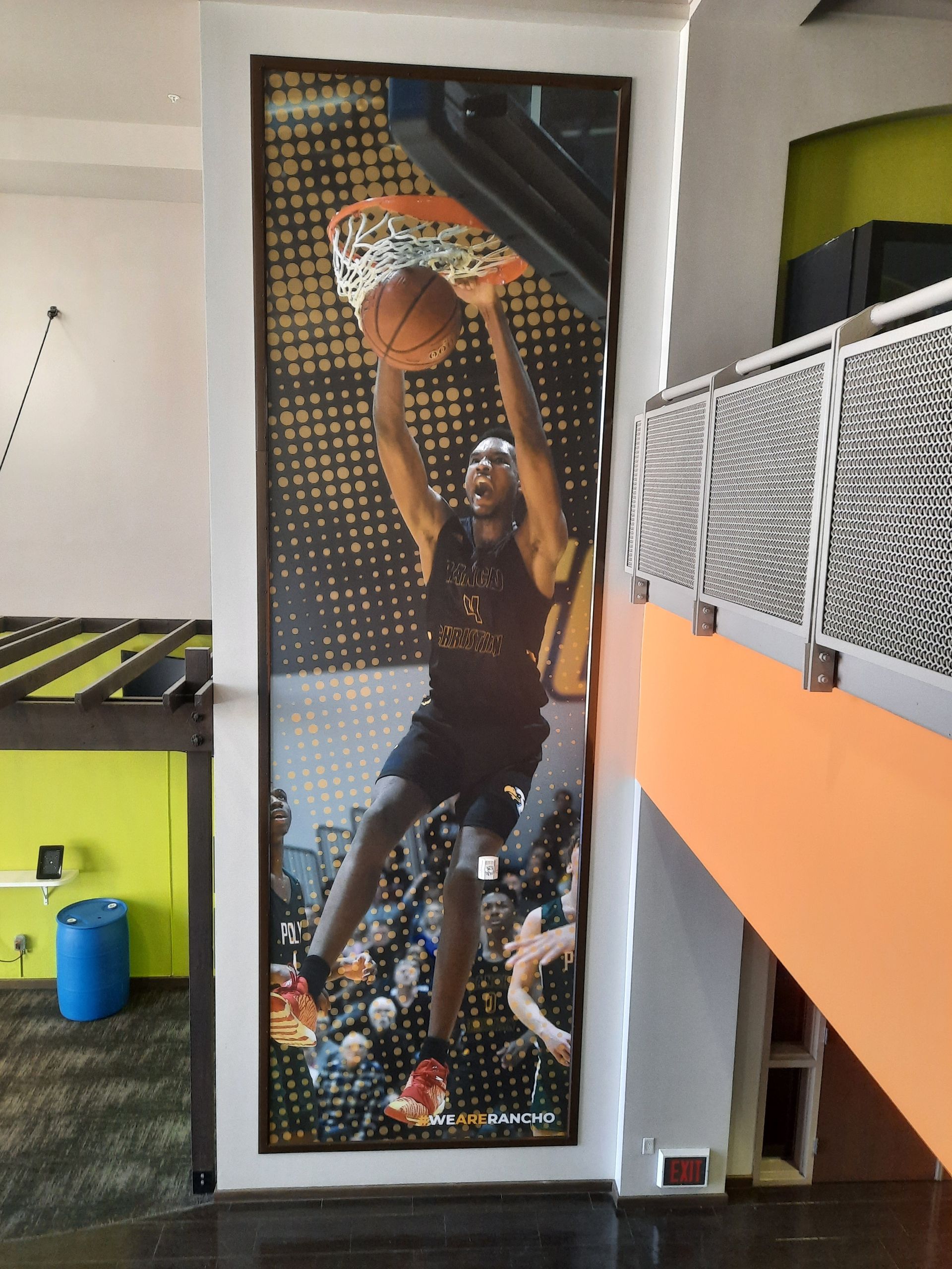 Indoor basketball mural beside a neon green arcade-style game area and orange loft railing.