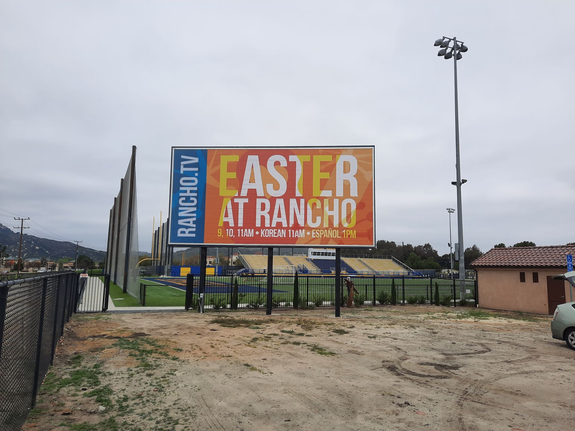 Easter at Rancho billboard near parking lot, with cloudy sky and palm trees in the background