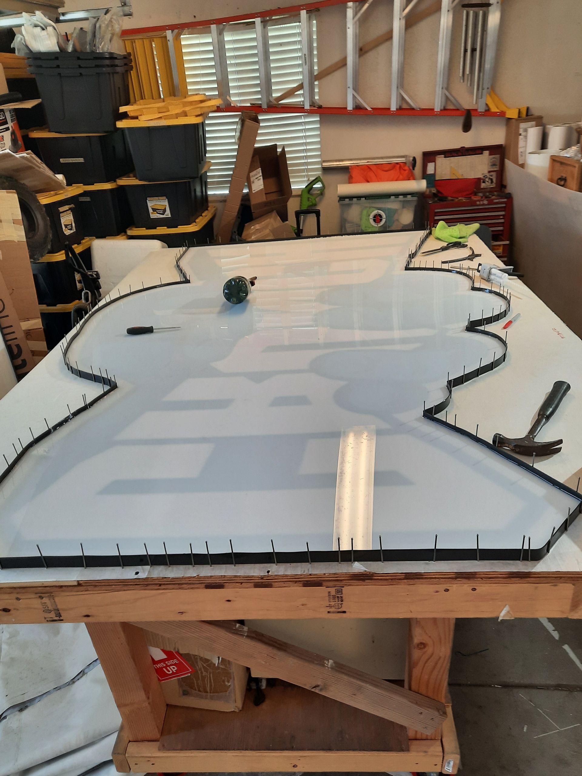 Large translucent sheet on a workbench in a cluttered workshop, with tools and clamps around it