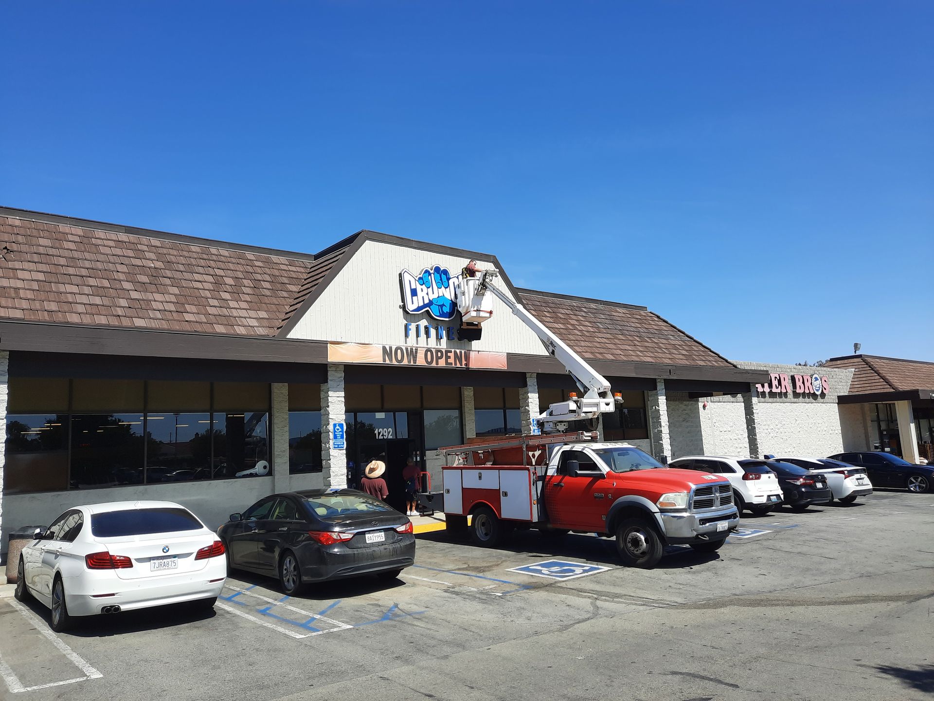 Strip mall storefront with parked cars and a red truck under a blue sky