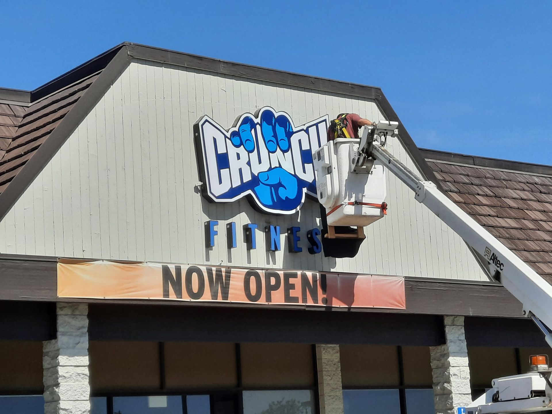 Crunch Fitness storefront with a “Now Open” sign under a blue sky