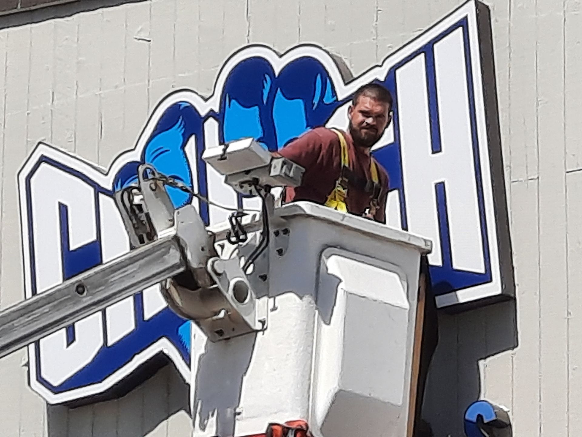 Man in a bucket lift working beside a large blue-and-white sign on a building