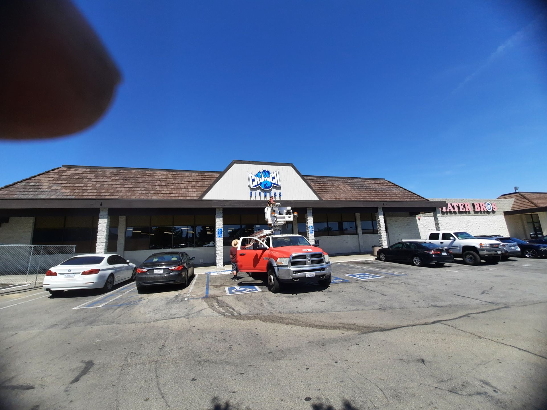 Strip mall storefront with parked cars under a bright blue sky.