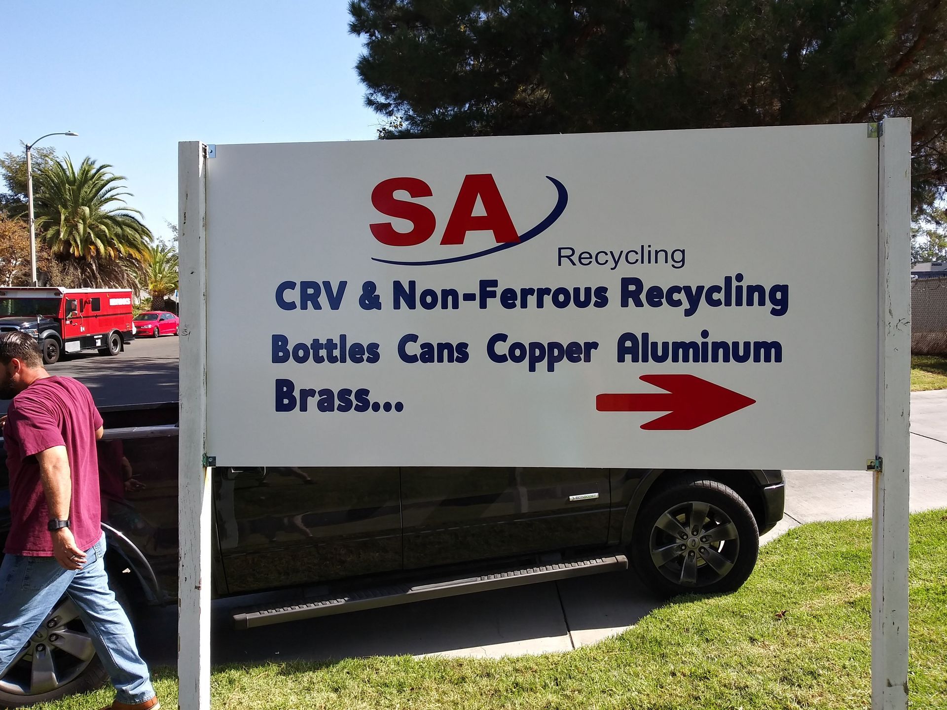 Recycling sign for bottles, cans, copper, aluminum and brass, with a red arrow outdoors