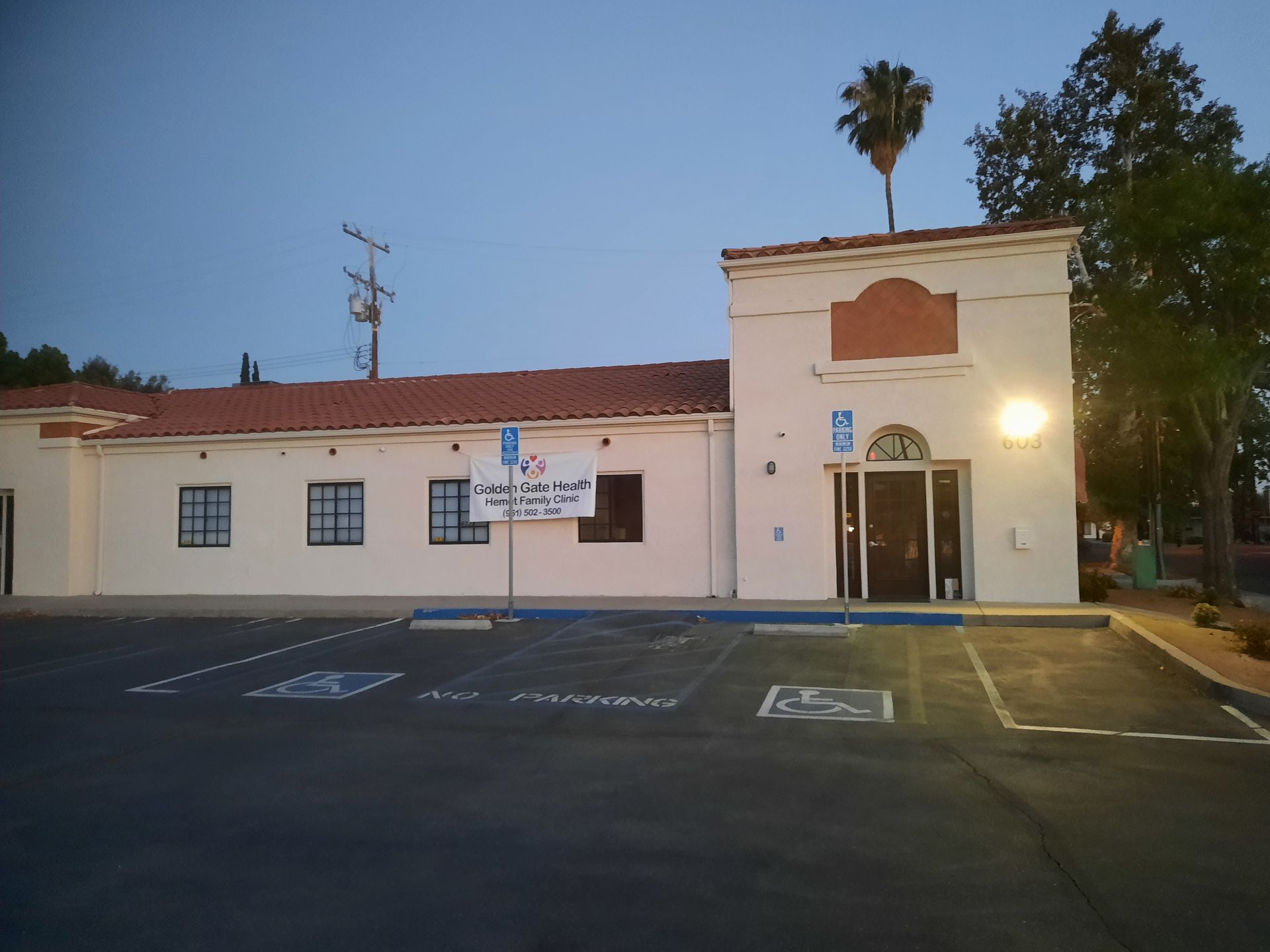 Small white building with red roof at dusk, with a lit doorway, parking lot, and handicap spaces in front