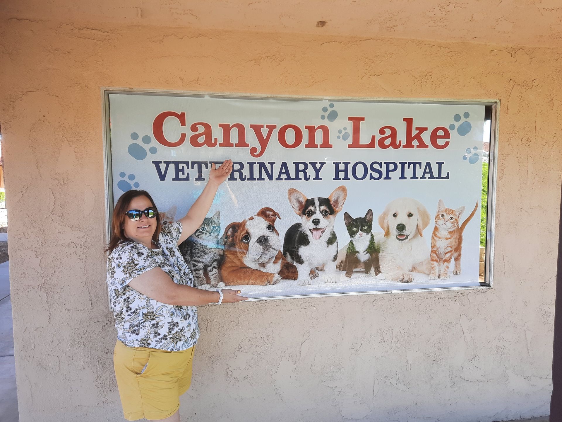 Woman pointing at Canyon Lake Veterinary Hospital sign with dog illustrations on a stucco wall