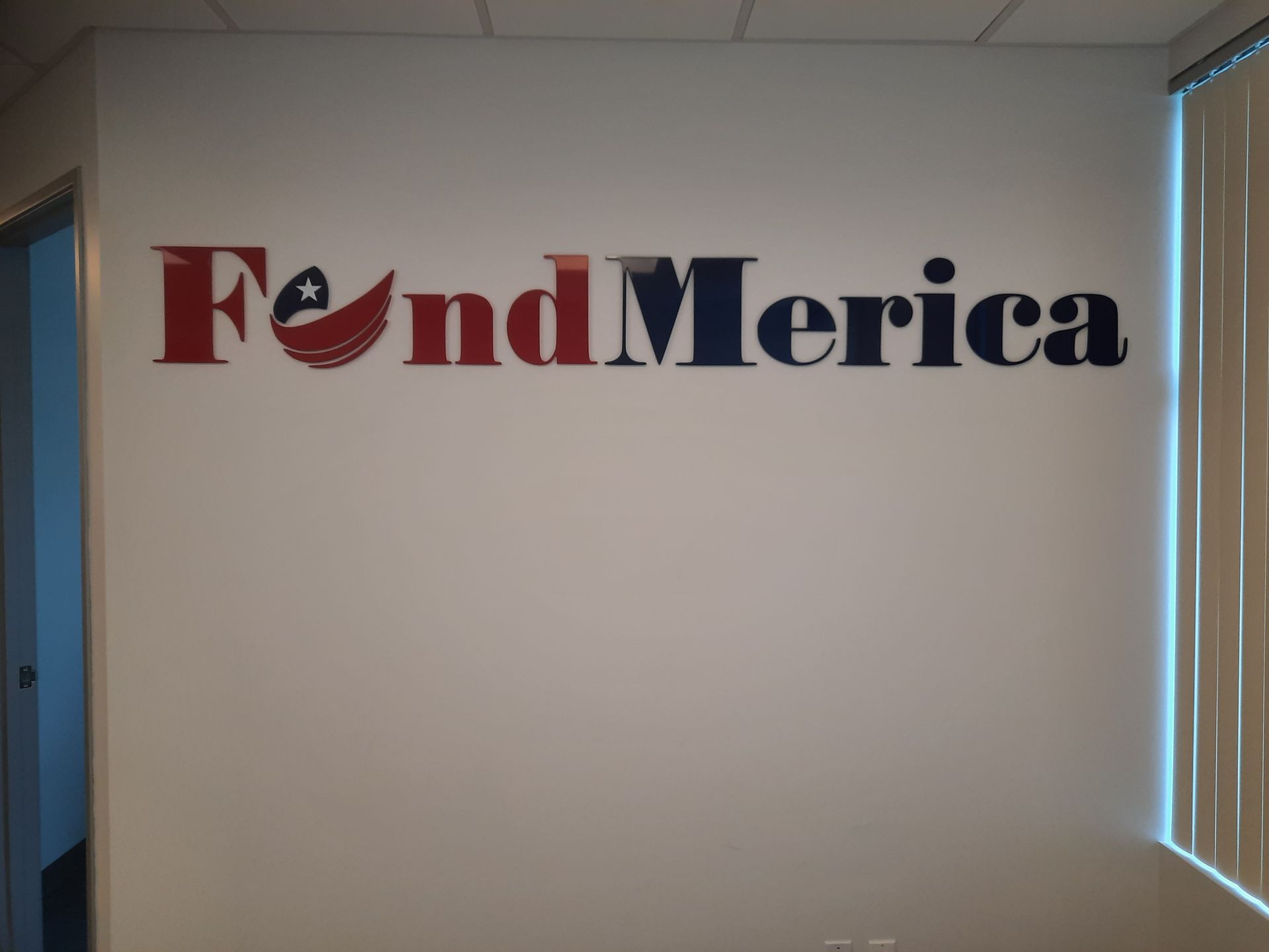 FondMerica logo on a white office wall near a window with vertical blinds