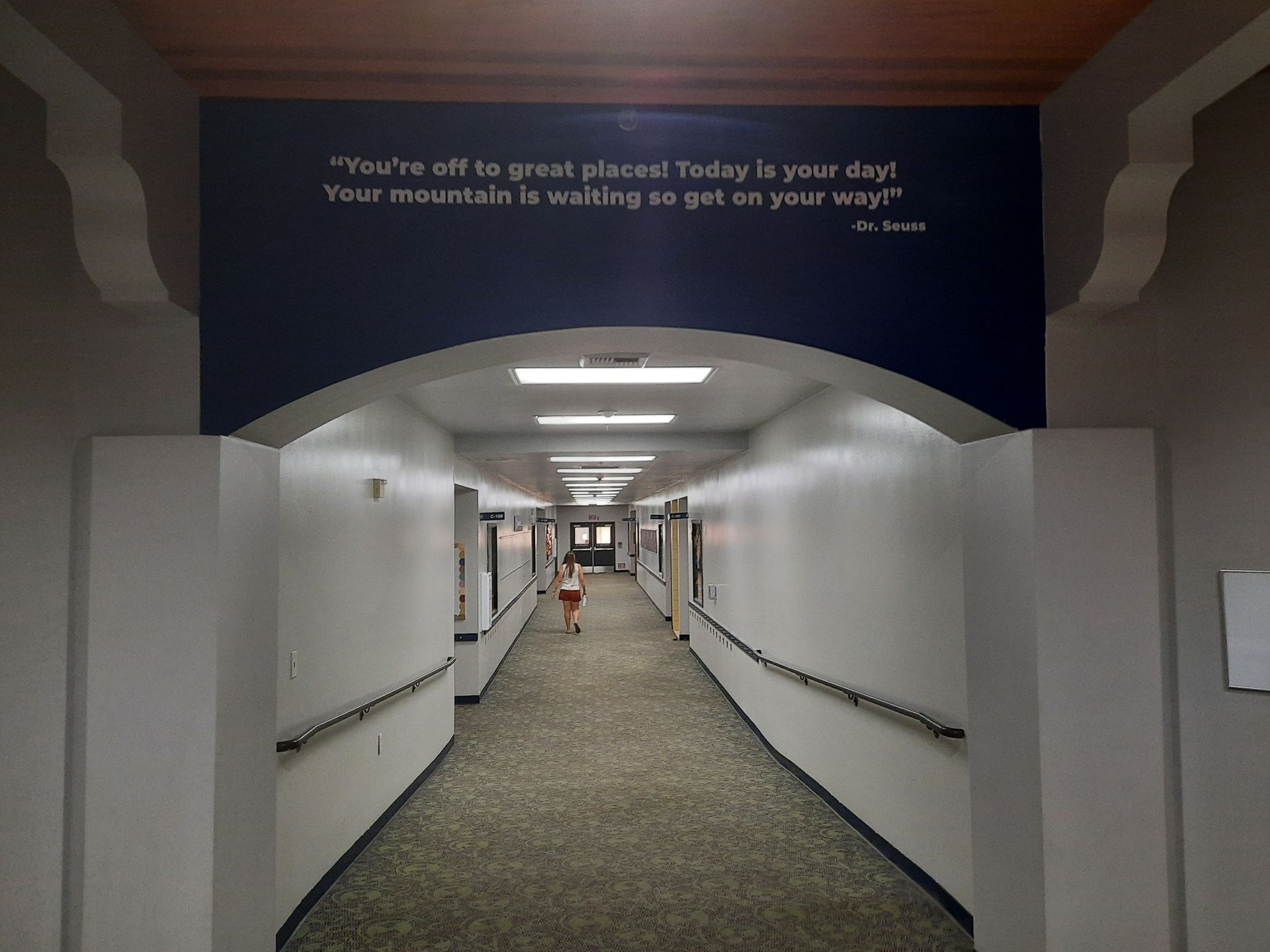 Long hallway with white walls, gray carpet, and a motivational quote on a dark blue archway.