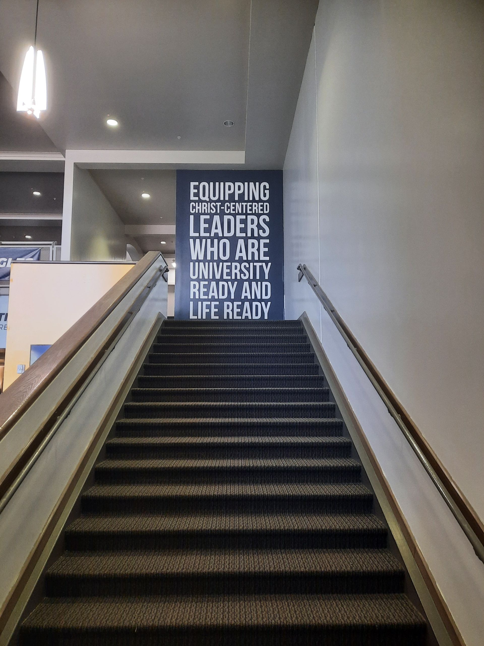 Staircase in a building lobby with a wall sign reading, “Educating others to be leaders who are ready to lead.”