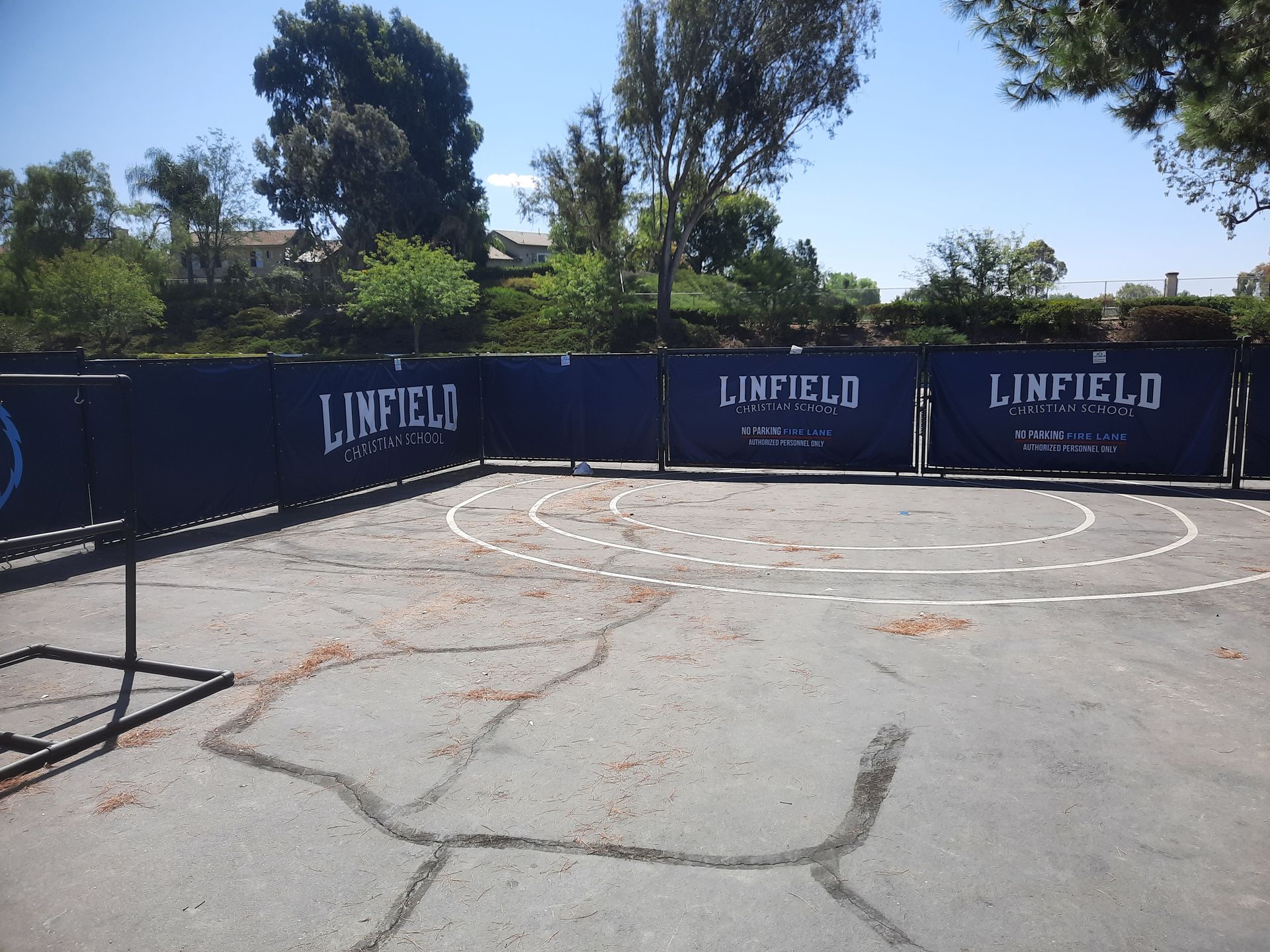 Empty outdoor court with blue barriers, cracked pavement, and trees under a sunny sky