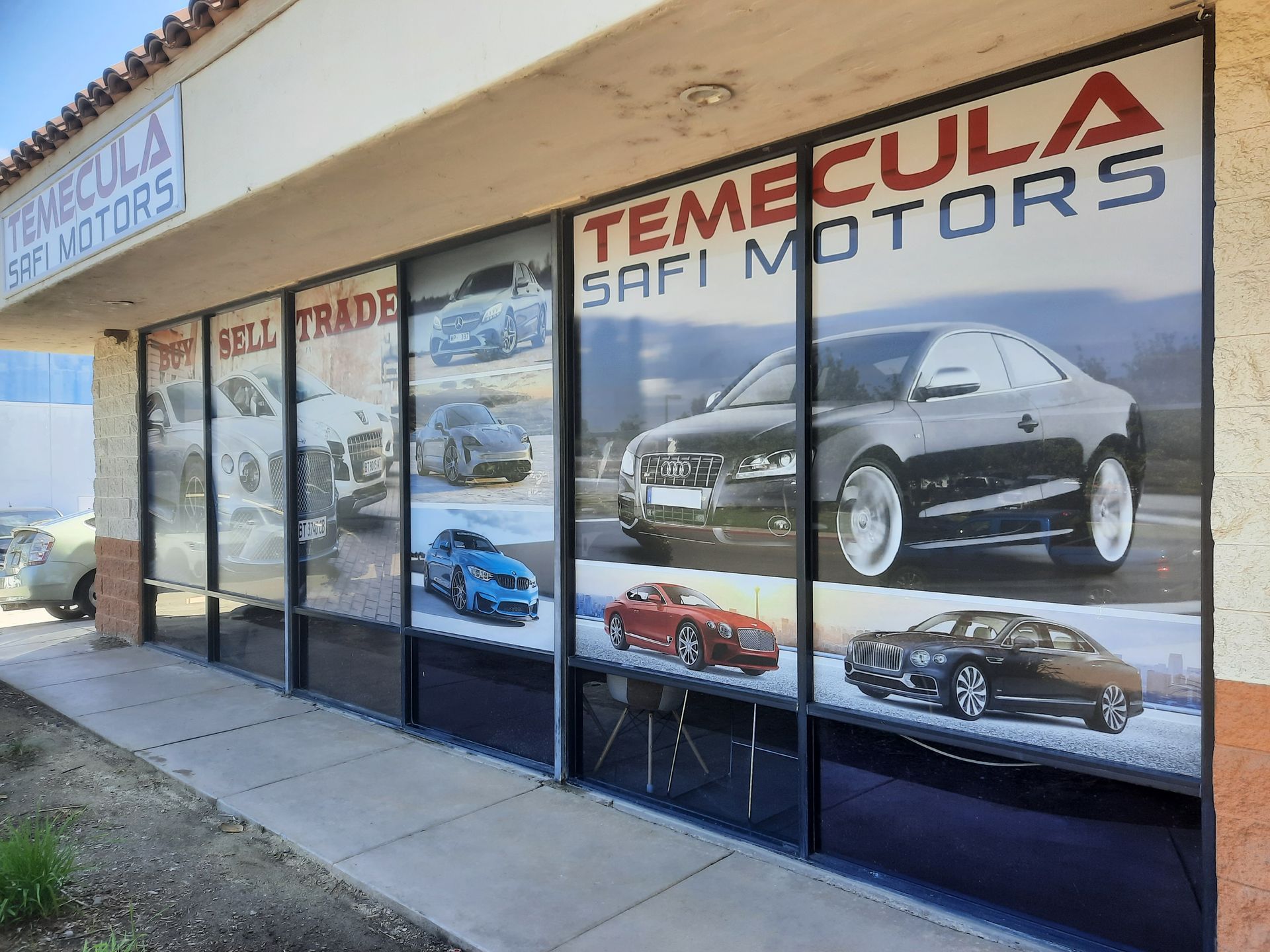 Temecula Safi Motors storefront with large car photos on window decals and sidewalk in front
