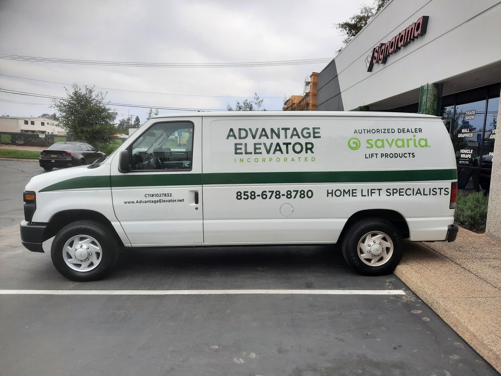 White Advantage Elevator service van parked outside a building, with business logos and contact number on the side