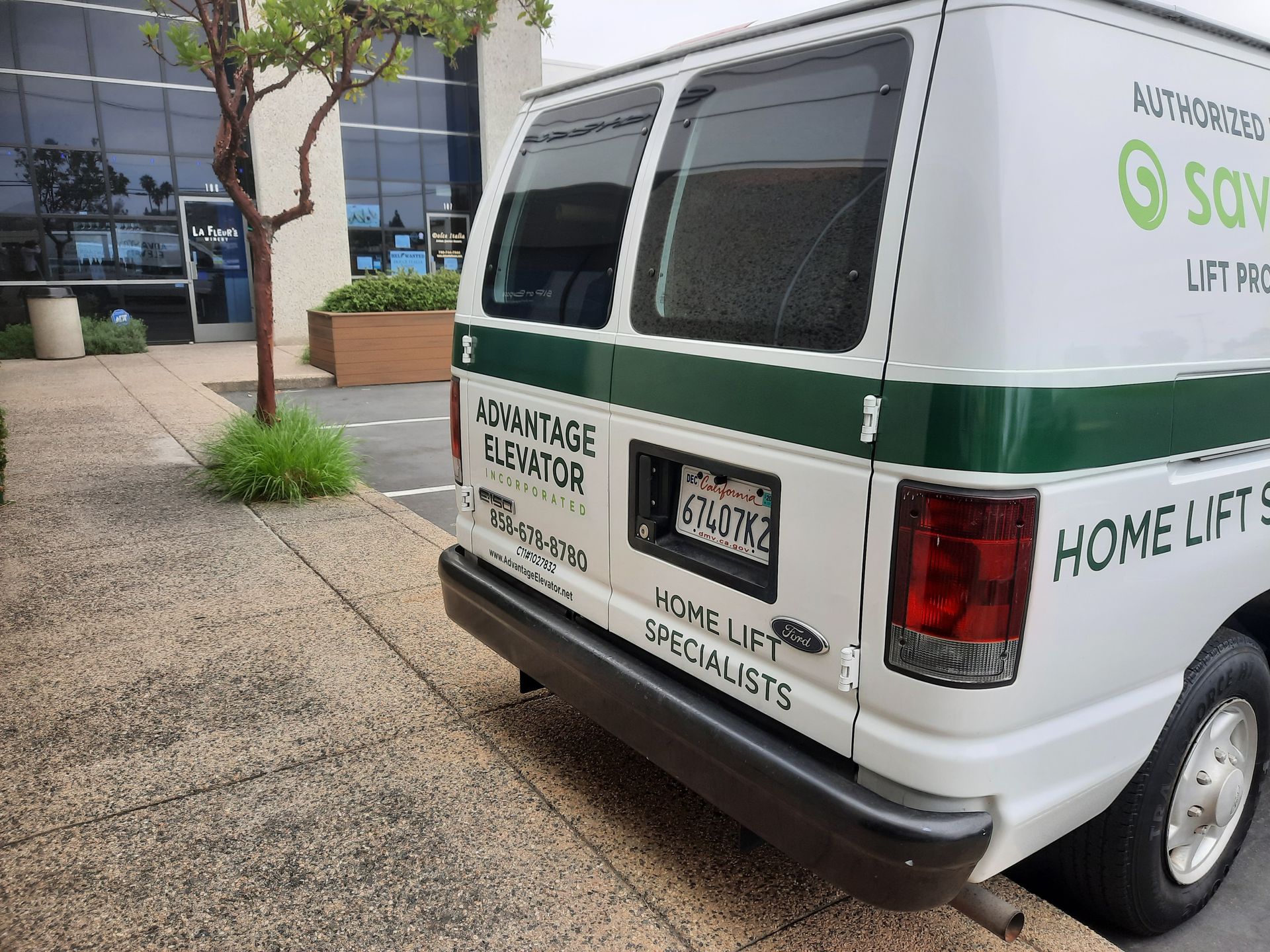 White-and-green home lift service van parked outside a building on a sidewalk, rear view.