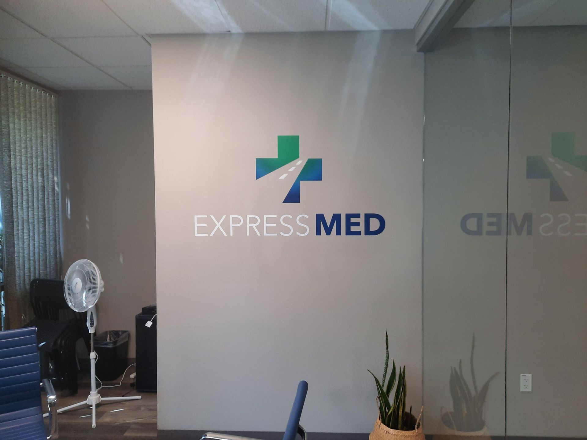 Express Med clinic reception wall with logo and plants in a glass-walled office