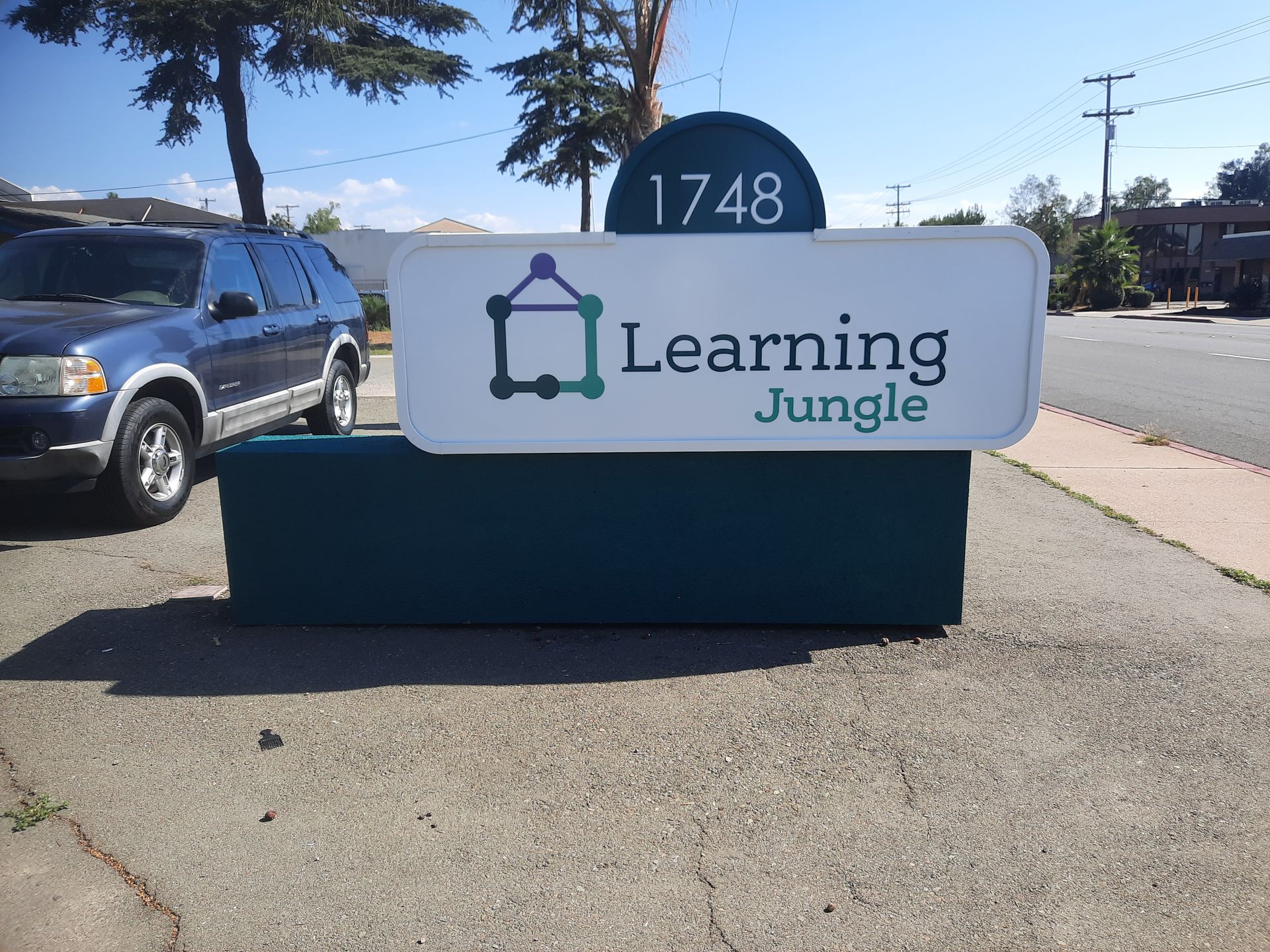 Learning Jungle daycare sign with building number 1748 beside a sidewalk and parked car under sunny skies