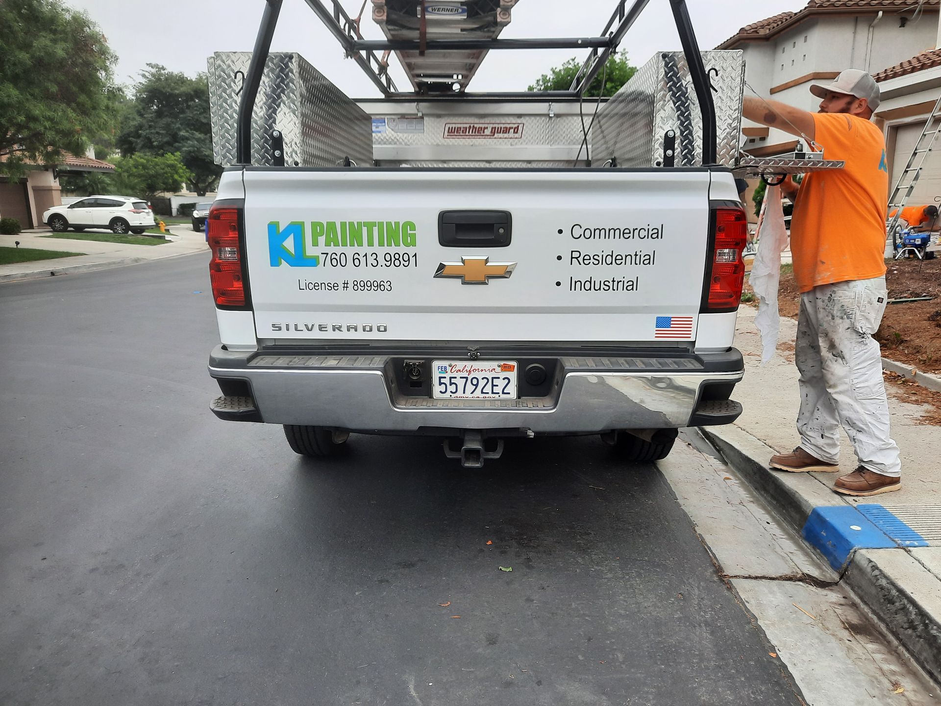 Worker spraying pavement behind white utility truck on wet street in a neighborhood