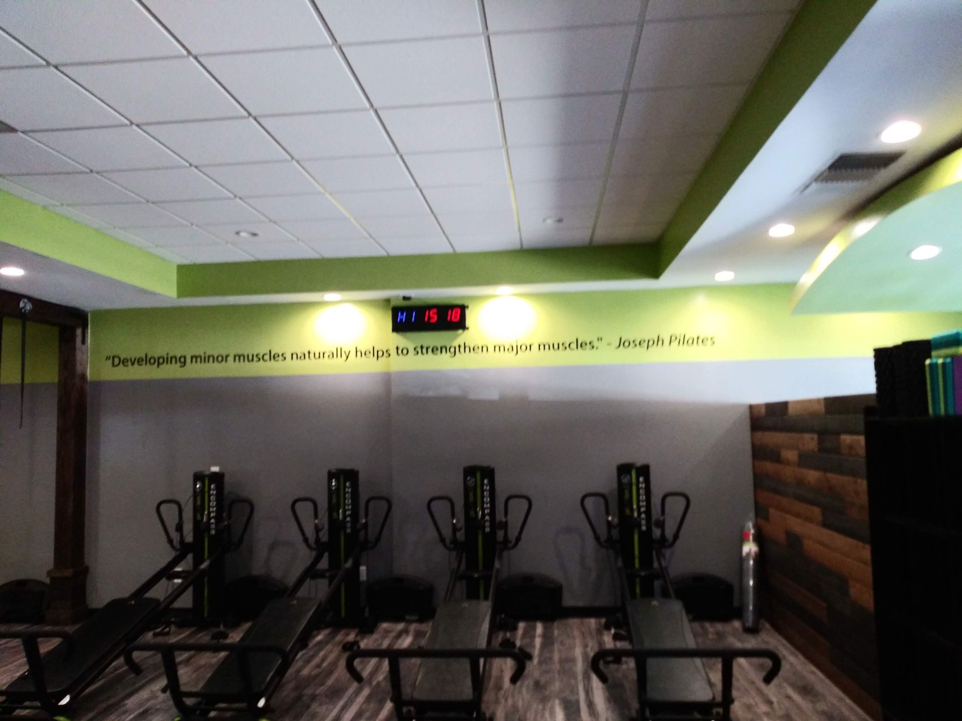 Gym with exercise equipment and wall-mounted digital clock under a green accent stripe.