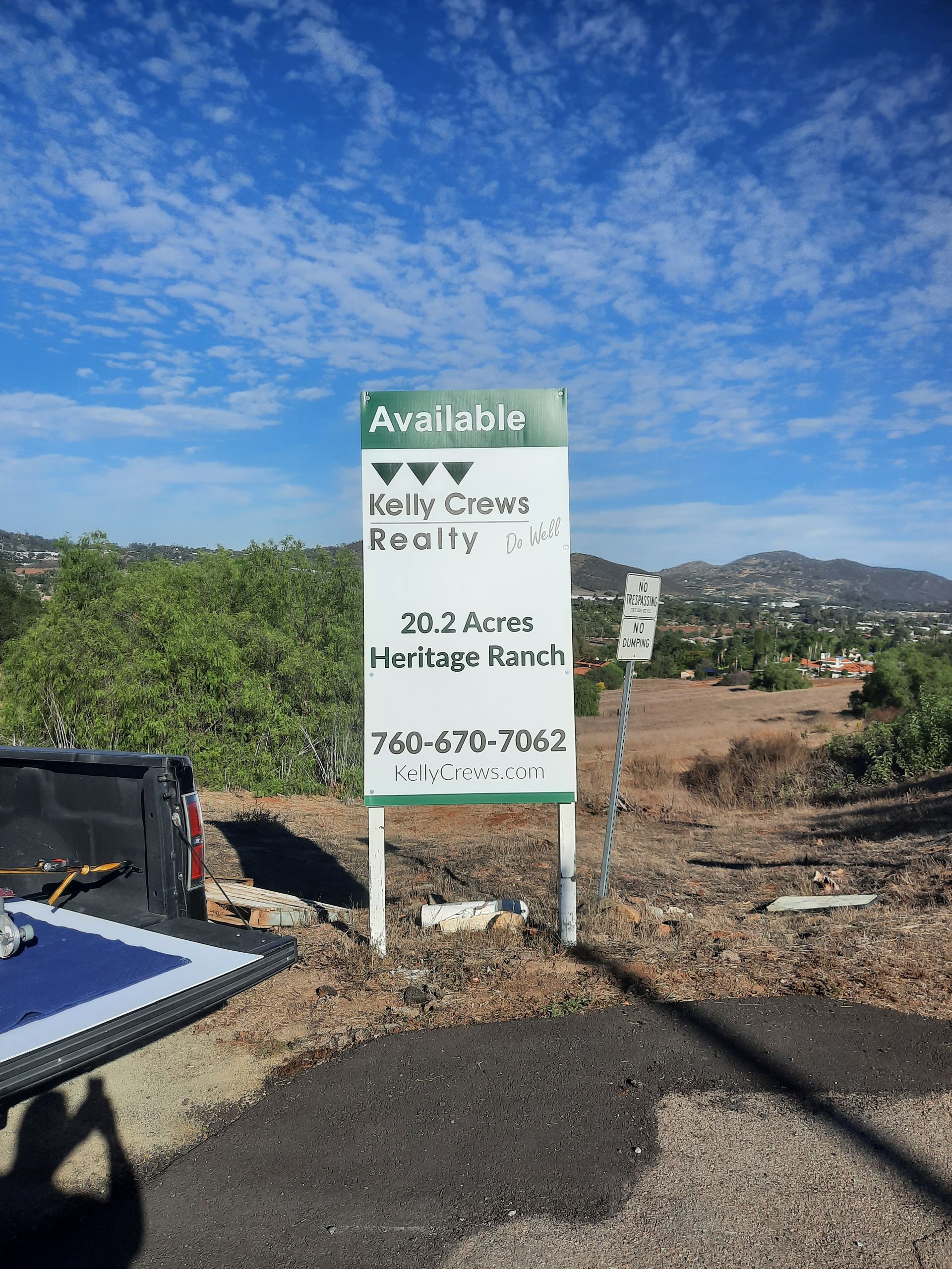 Realty sign at a vacant lot under blue sky, with mountains in the background
