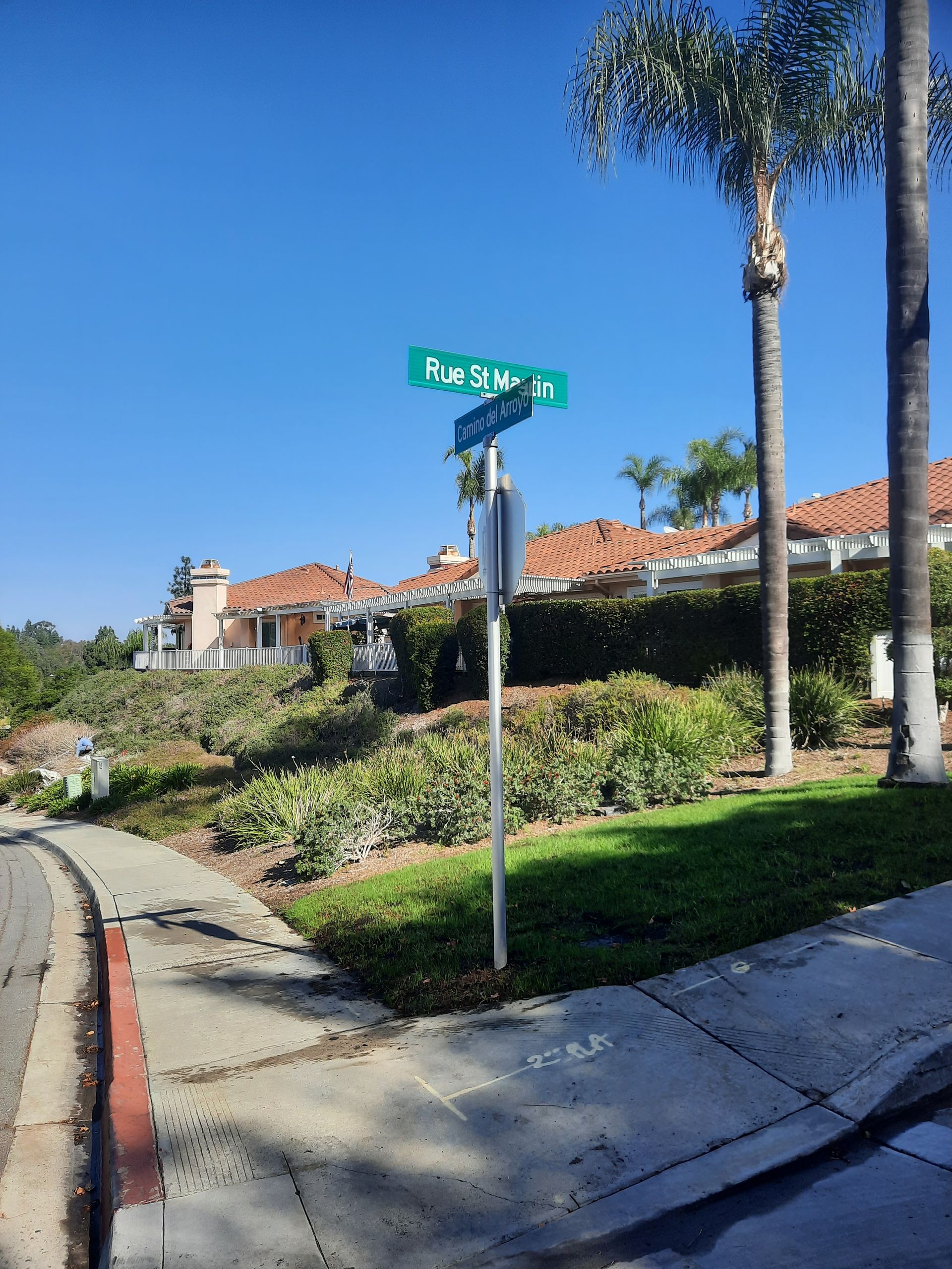 Street sign at a sunny suburban corner with palm trees and red-roofed houses in the background