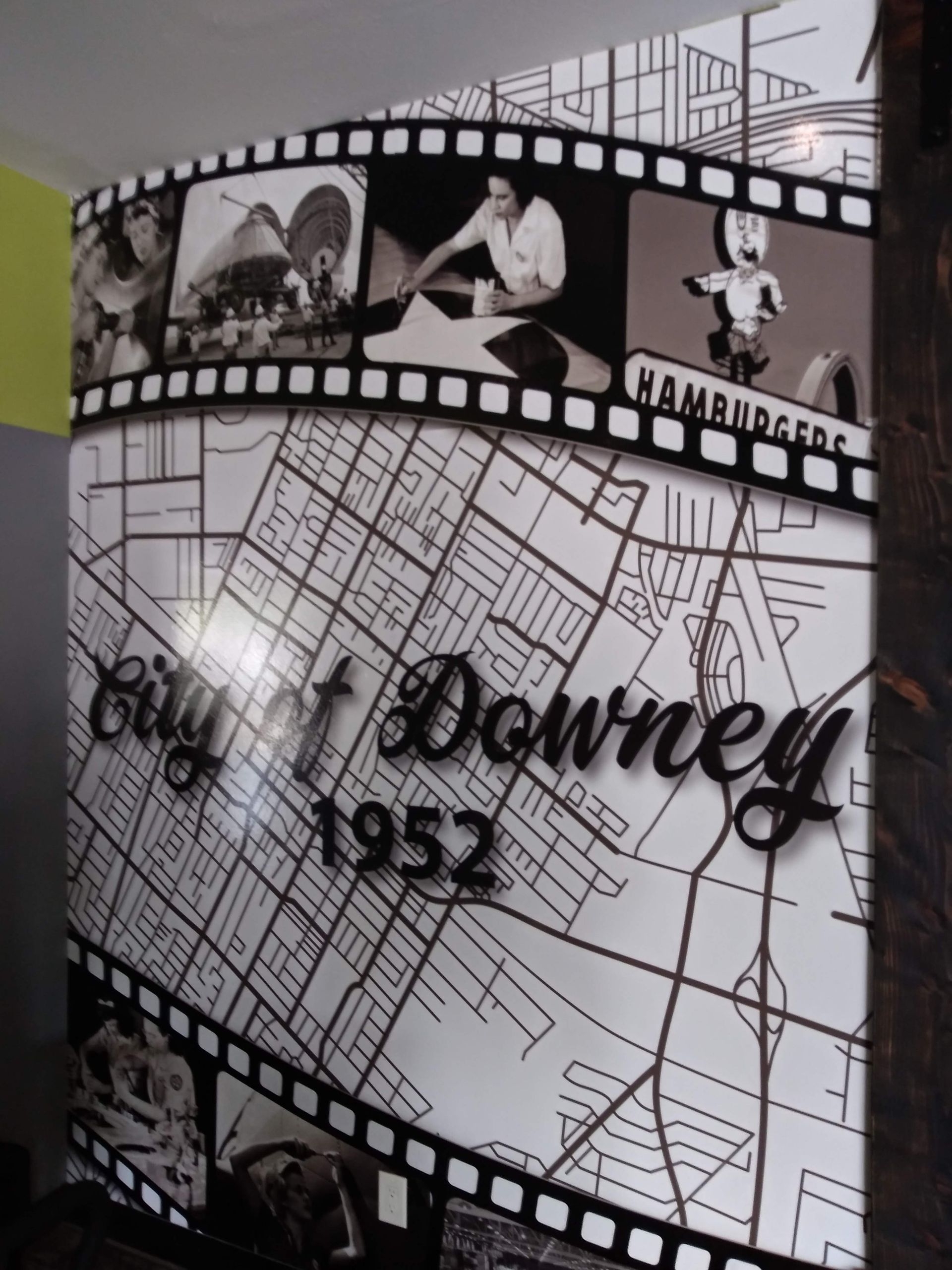 Black-and-white wall graphic with filmstrip photos and map background, labeled “Clint Downey 1952.”