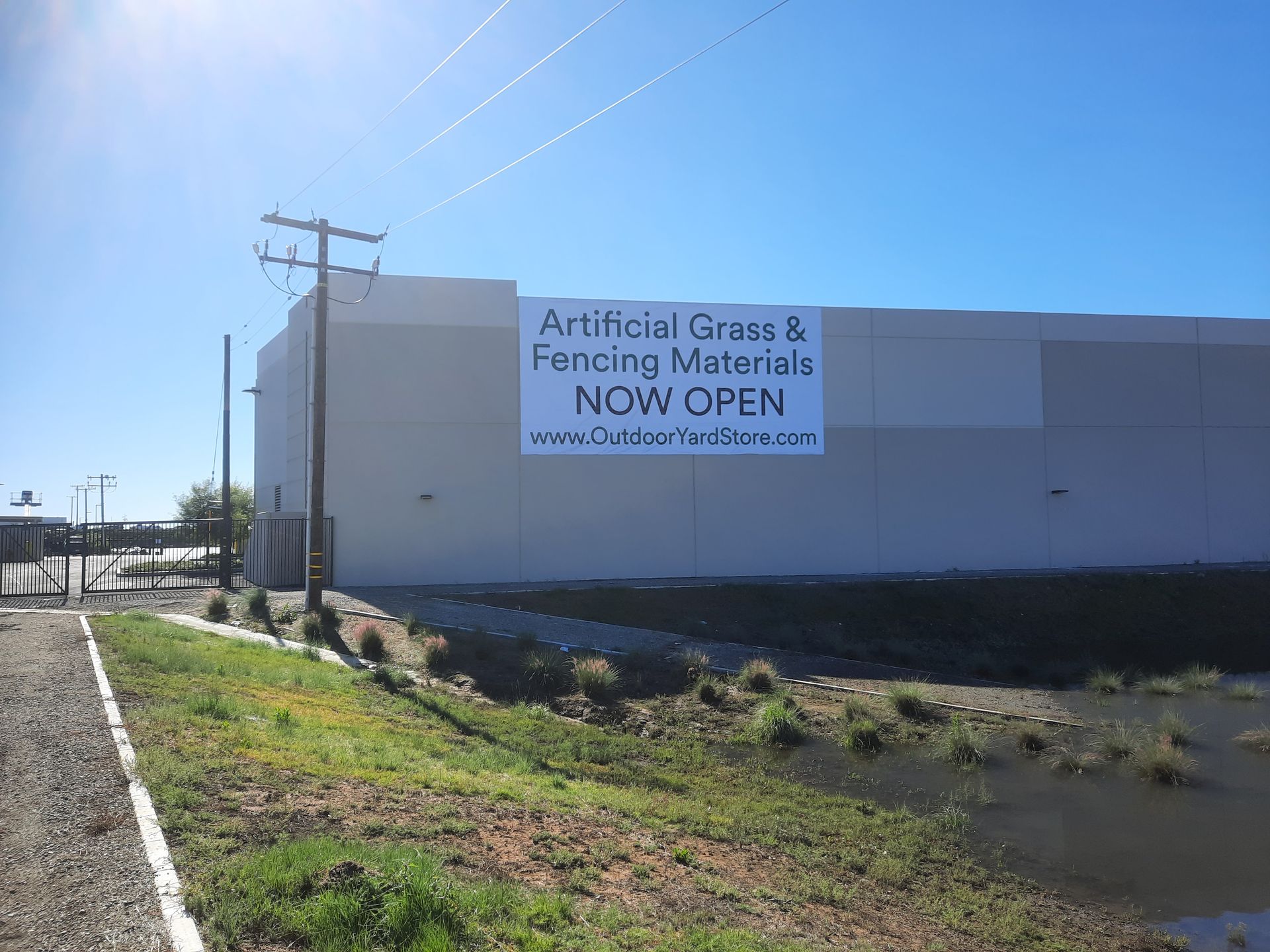 Street view of a white building with a “NOW OPEN” sign under a bright blue sky