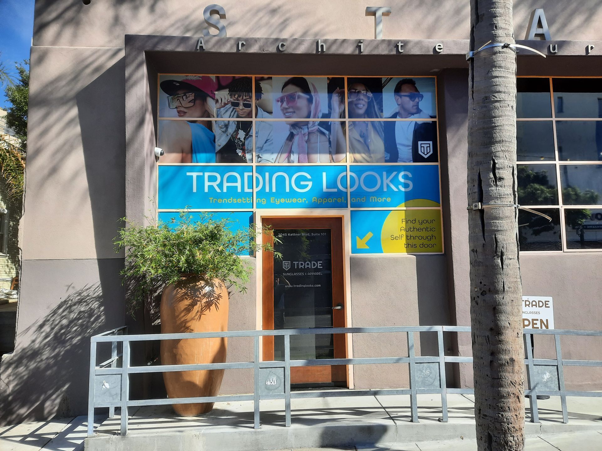 Storefront for “Trading Looks” with blue sign, entrance, and palm trees outside