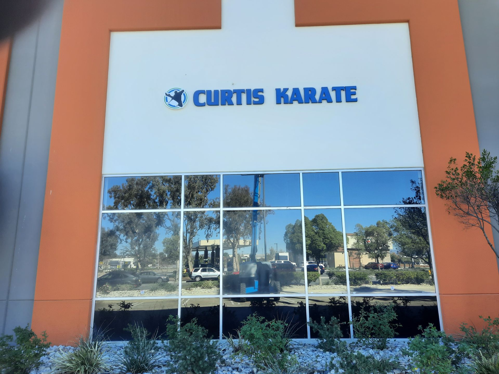 Curtis Karate storefront with blue sign on white facade and orange walls, reflected in front windows