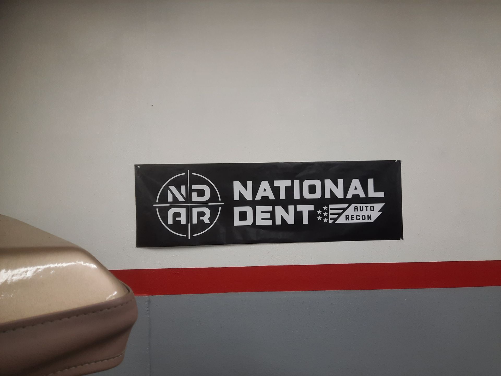 Black National Dent sign on a beige wall above a red stripe, beside a dental chair.