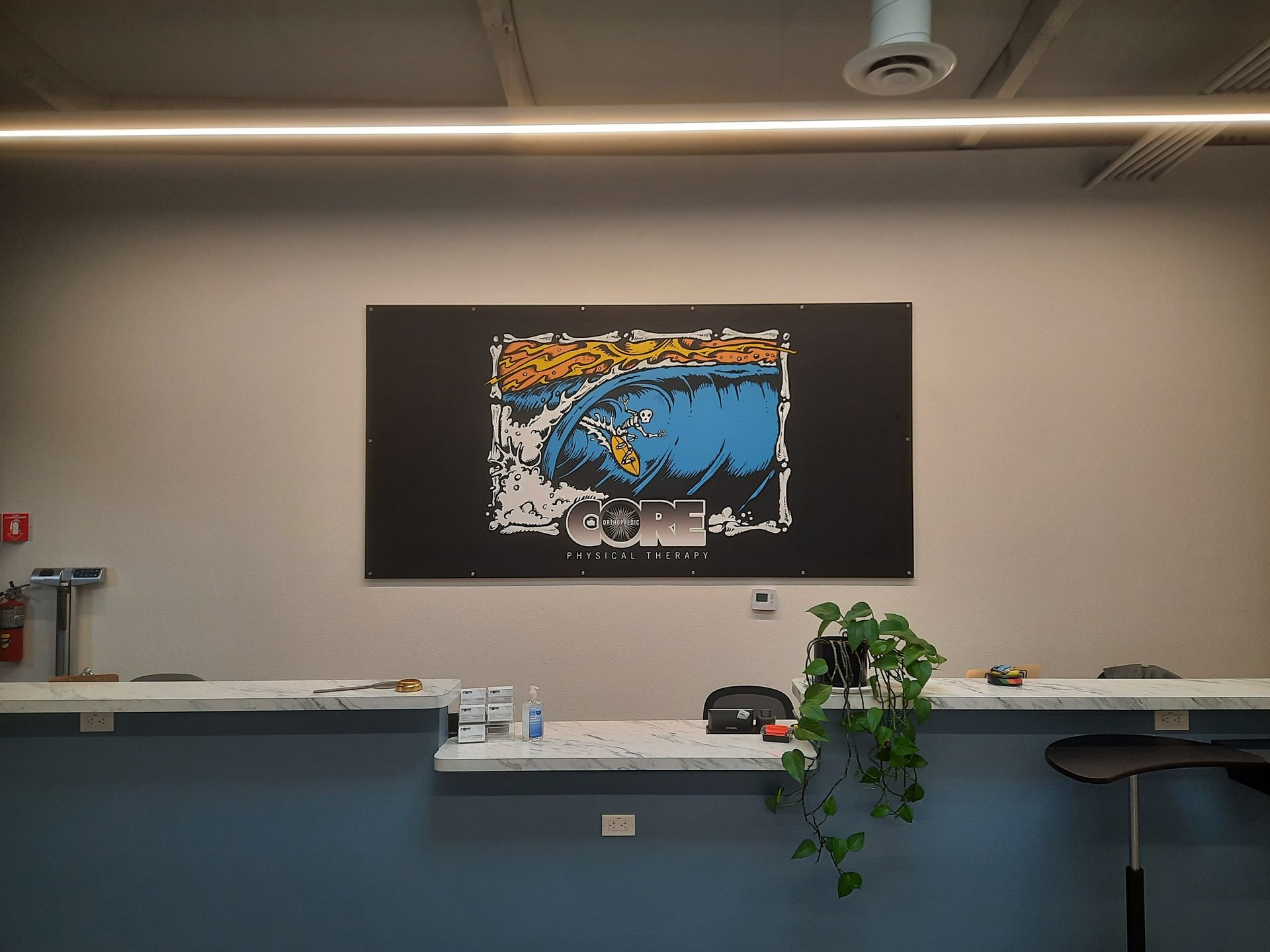 Modern room with a long counter, potted plant, and abstract wall art above a blue reception desk.