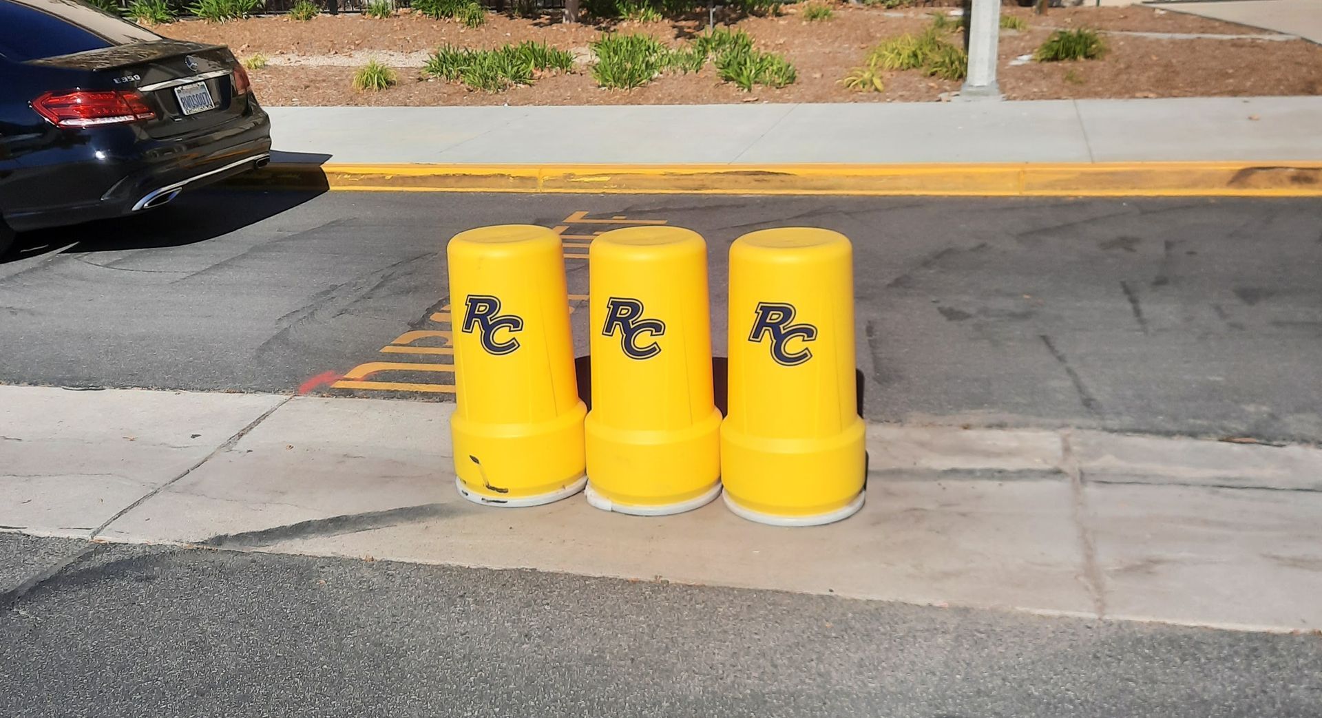 Three yellow bollards with black markings on a curb beside a street and parked car