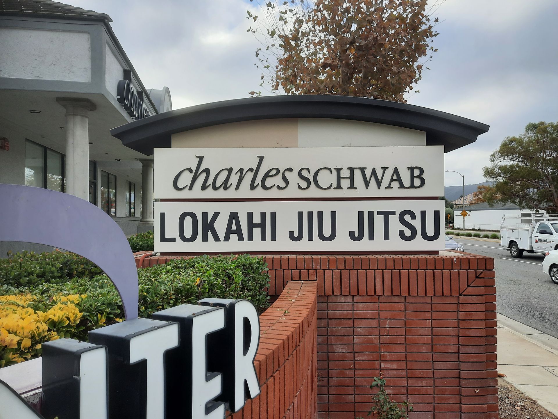 Charless Schwab sign above Lokahi Jiu Jitsu at a brick entrance, with flowers and a purple sculpture nearby