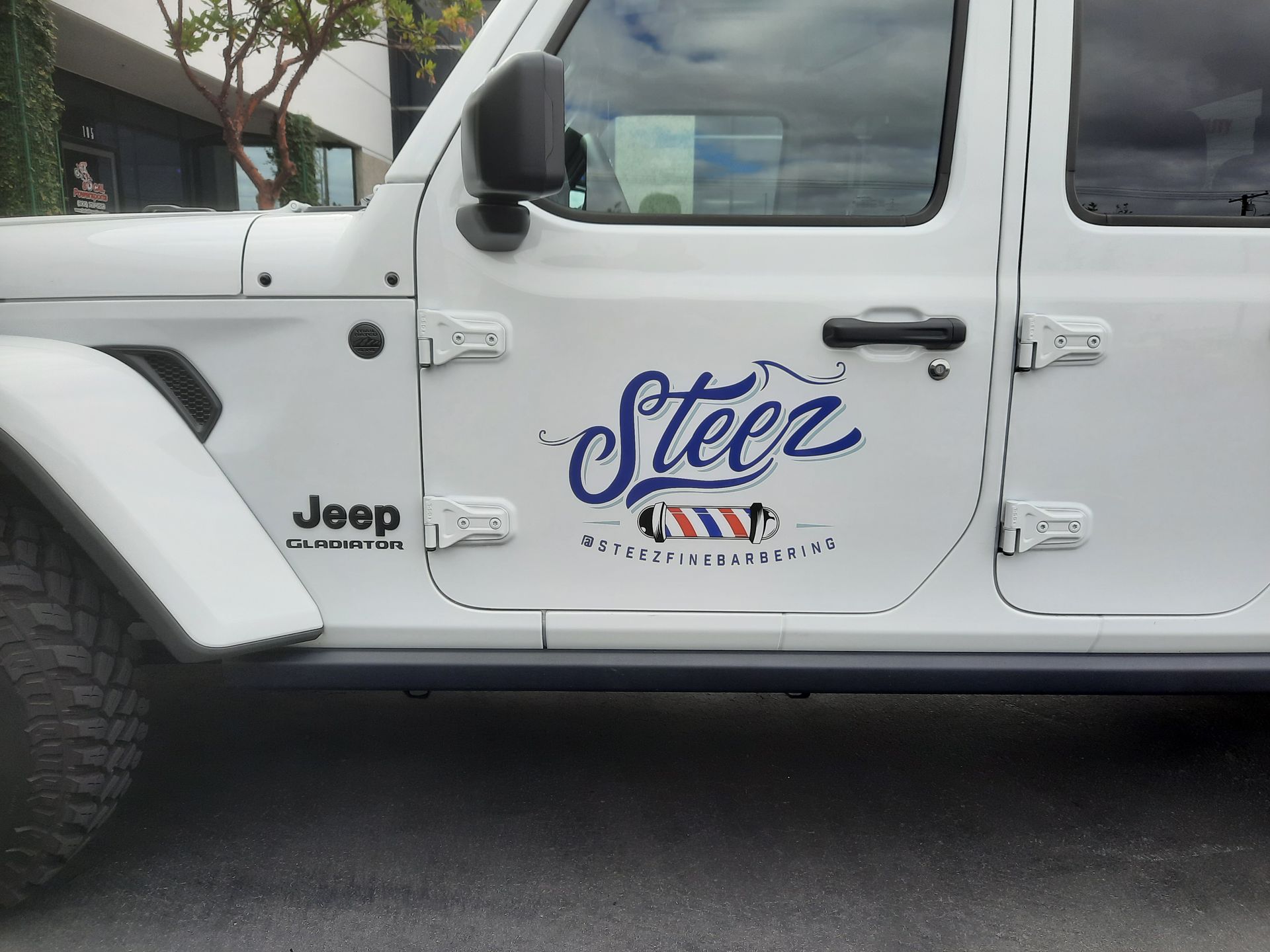 White Jeep Wrangler with a blue-and-orange “steez” logo on the door, parked outdoors.
