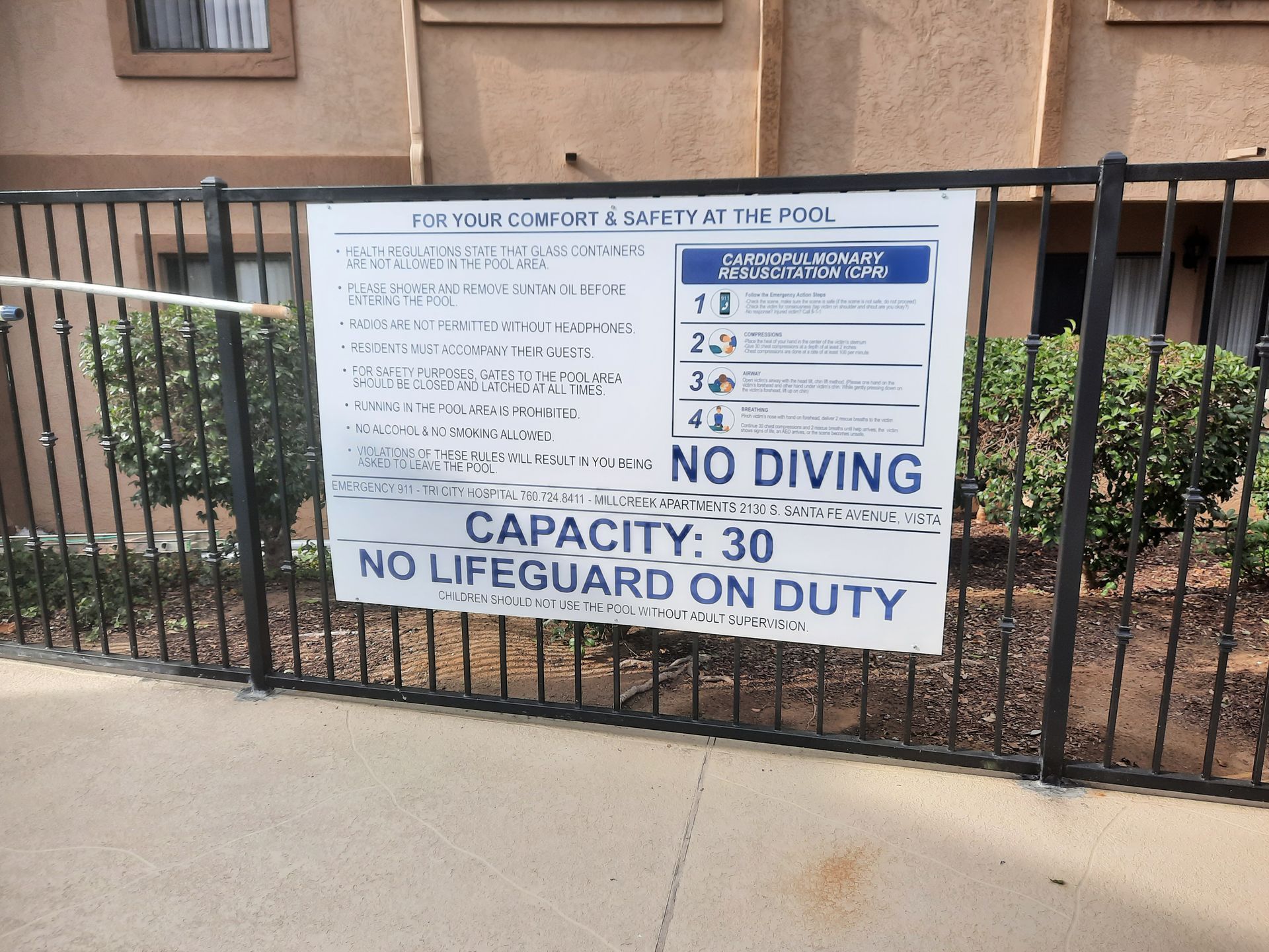 Pool rules sign on fence: capacity 30, no lifeguard on duty.