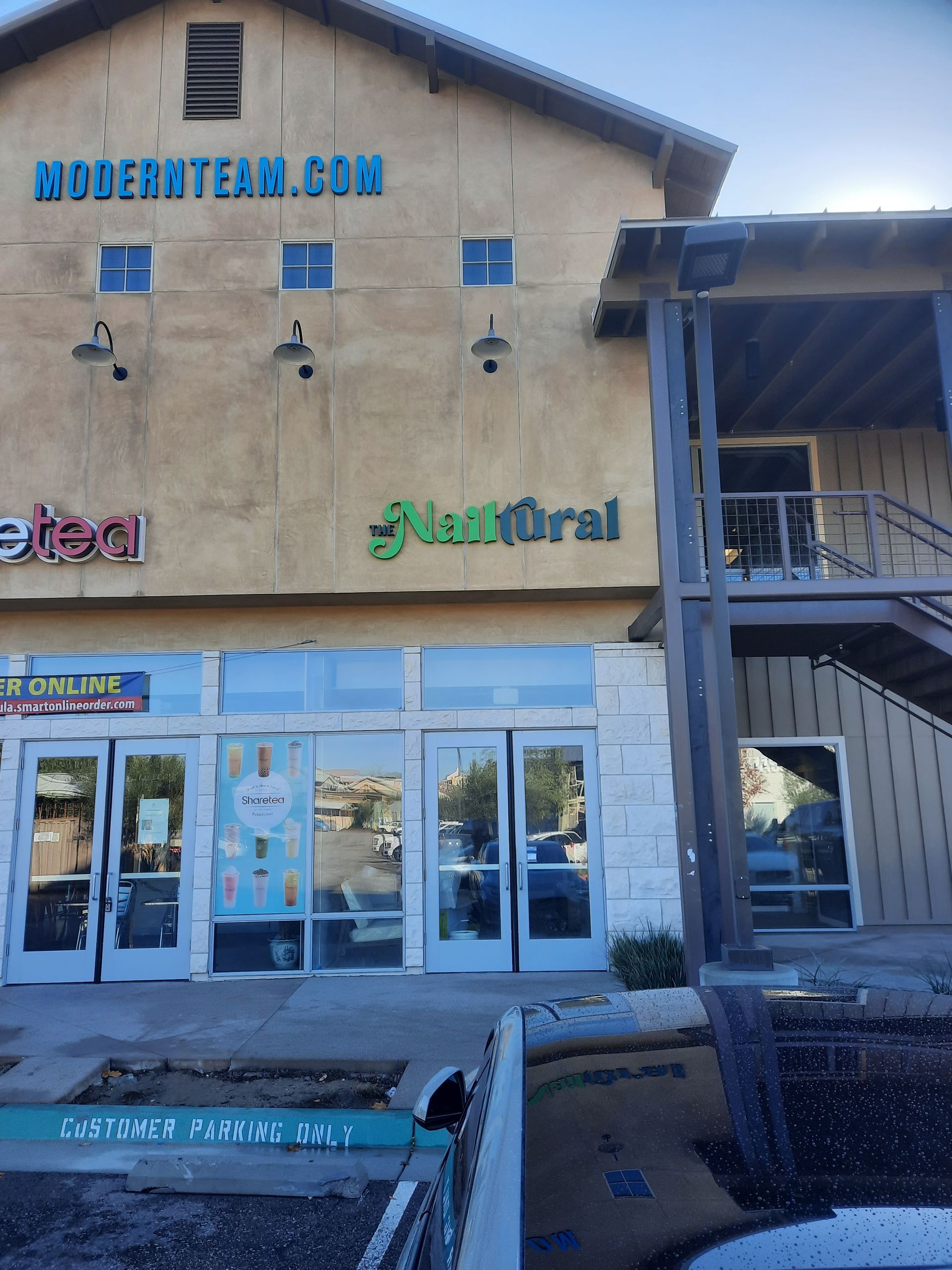 Retail storefront with blue doors and tan siding, featuring Henderson.com and floral signs under a covered walkway
