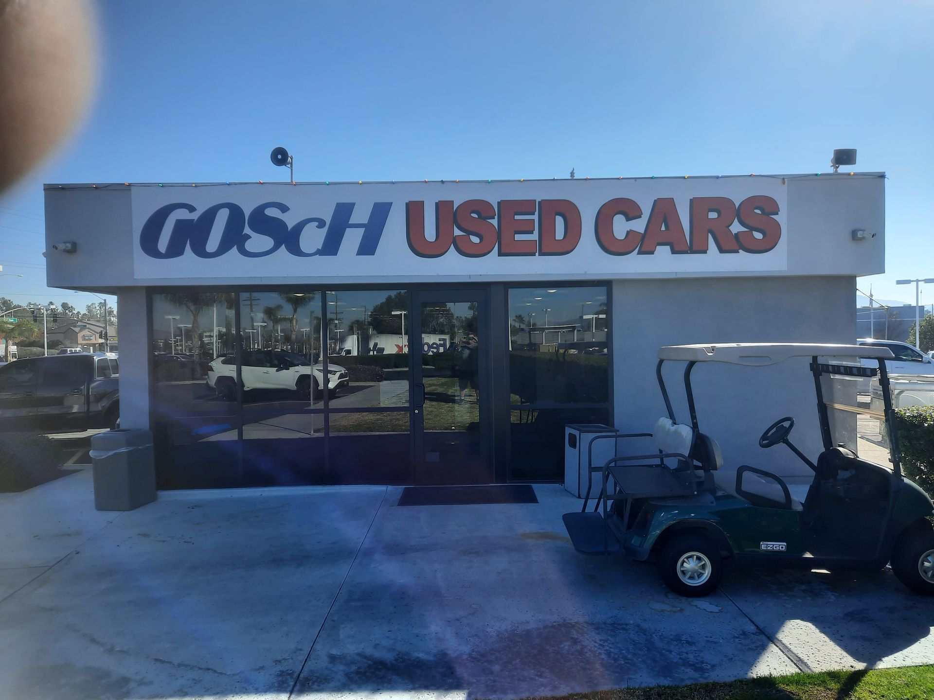 Gosch Used Cars storefront with glass windows and a golf cart parked outside