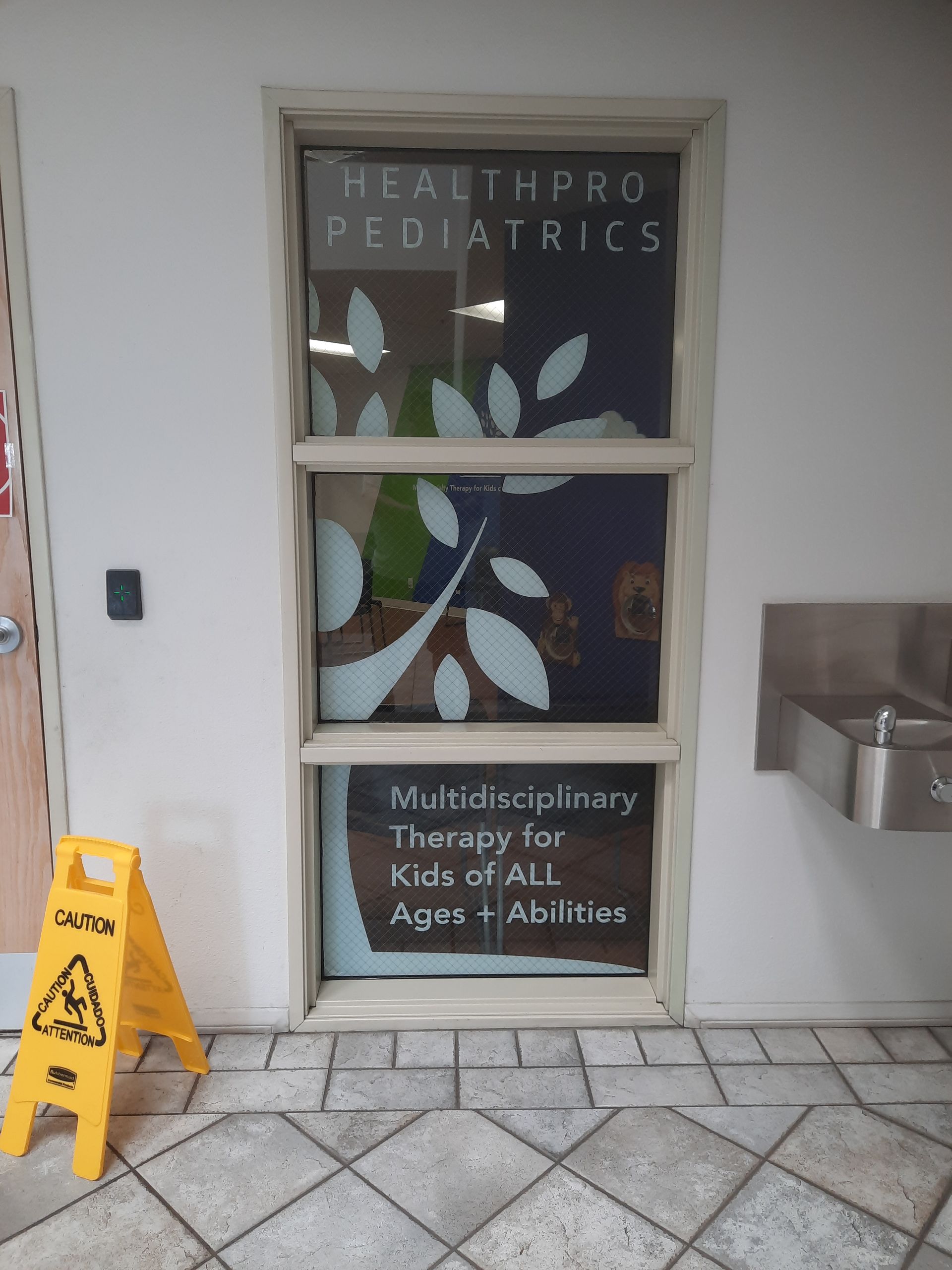 HealthPro Pediatrics office window with floral decals and a wet floor caution sign
