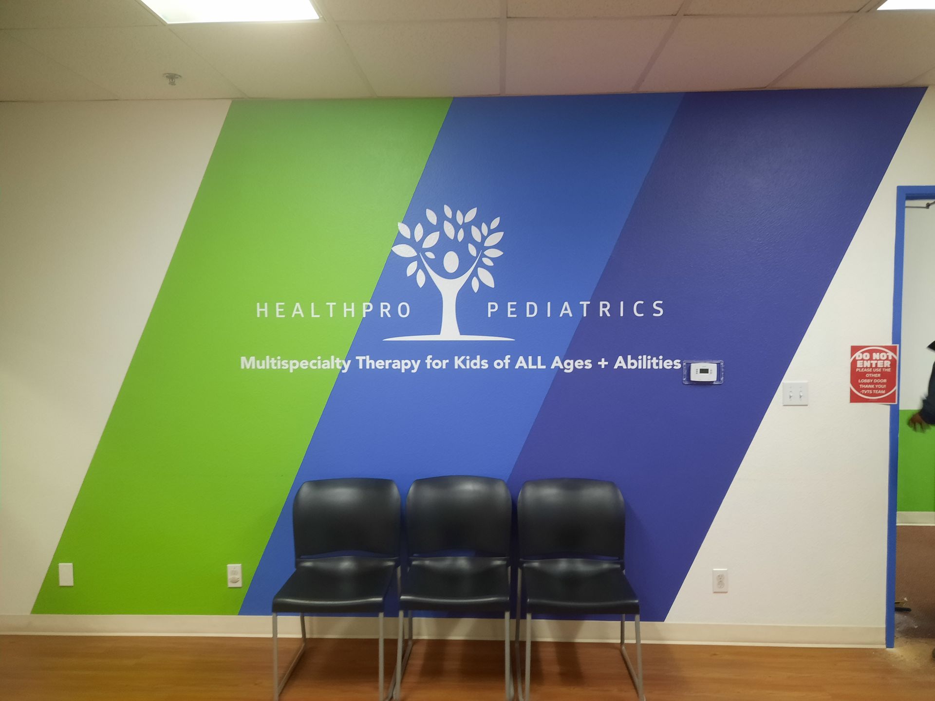 Waiting area with three black chairs in front of a green and blue HealthPro Pediatrics wall.