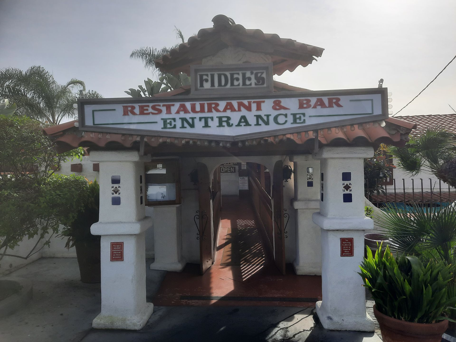 Entrance to FIDES Restaurant & Bar with white pillars, tile roof, and greenery around the doorway