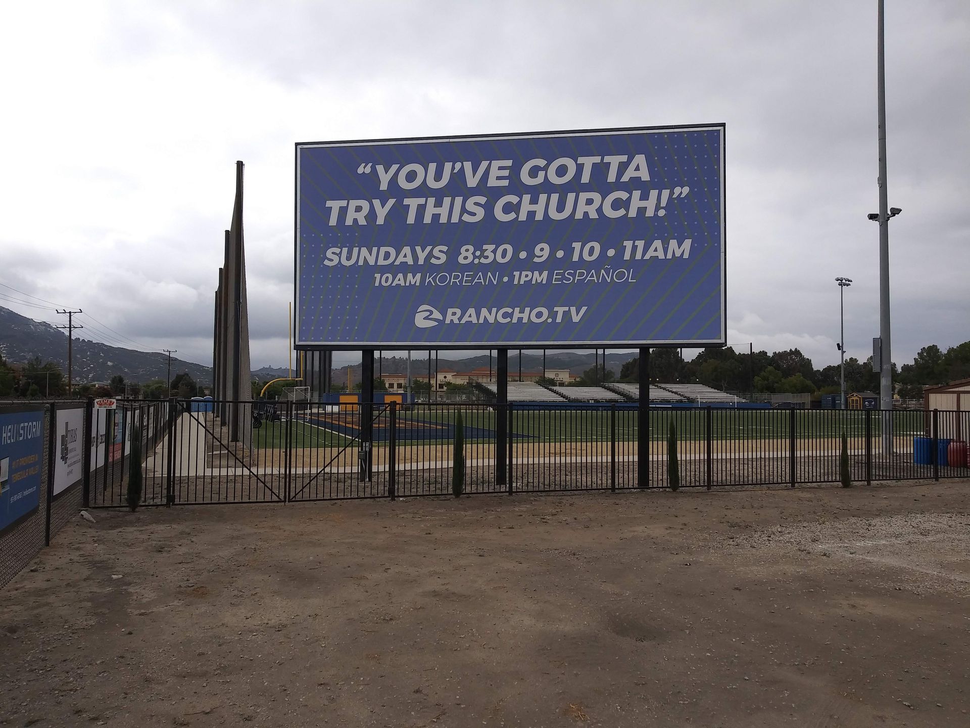 Billboard at a baseball field reads, “YOU’VE GOTTA TRY THIS CHURCH!” with Sunday service times.