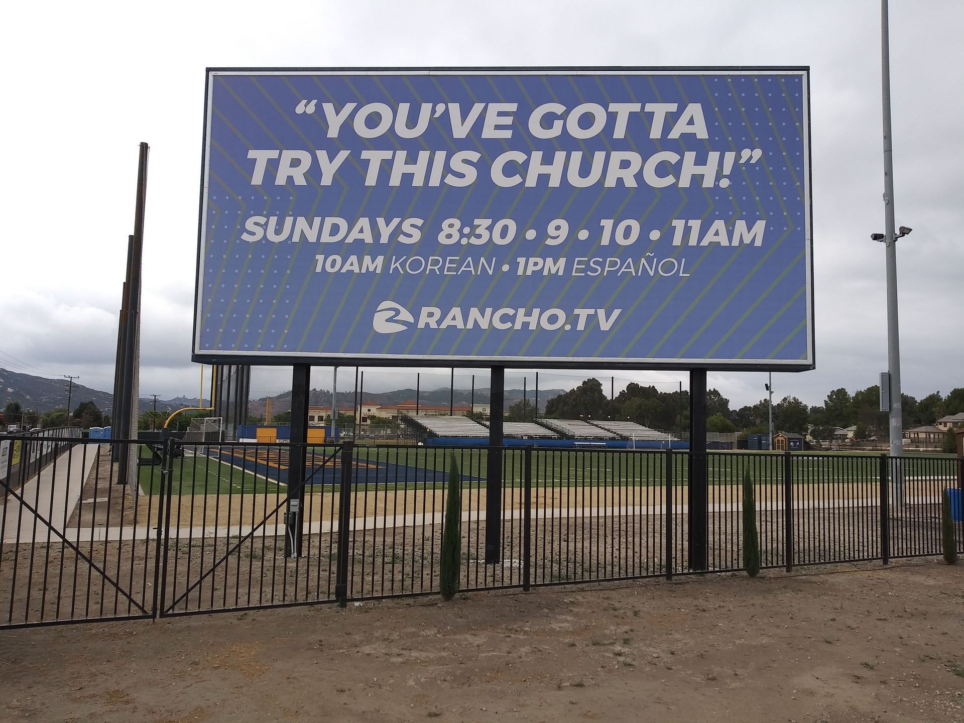 Billboard by a fenced field reads, “You’ve gotta try this church!” with Sunday service times.