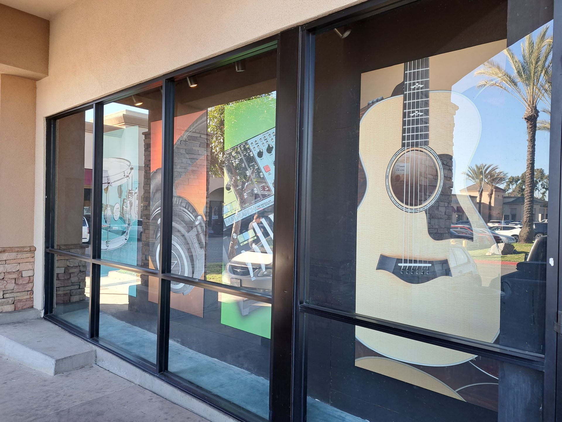 Storefront windows with large guitar graphics and reflections of a street scene.