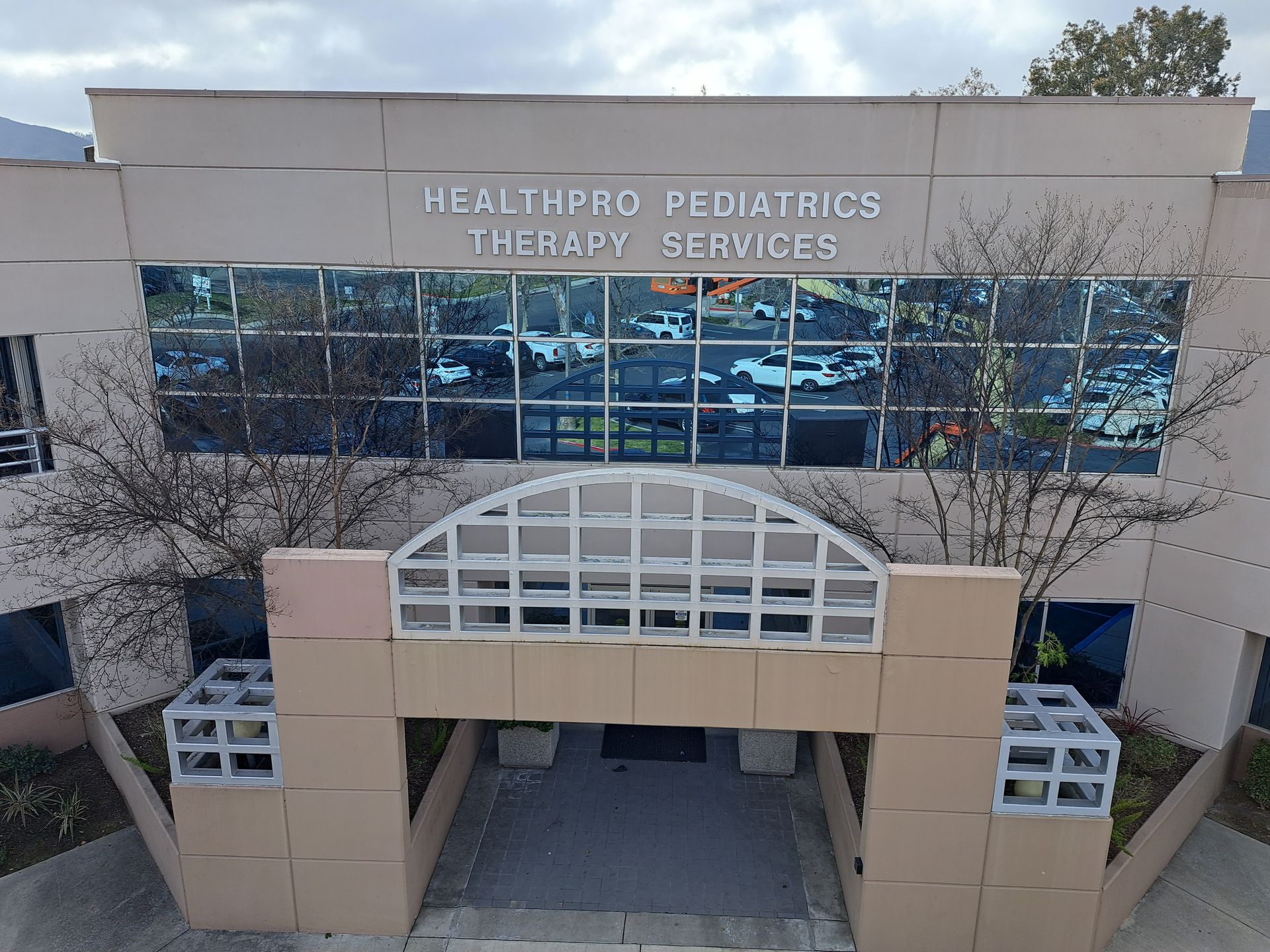 Front entrance of a healthcare building with beige facade and blue windows labeled “Healthpro Pediatric Therapy Services”