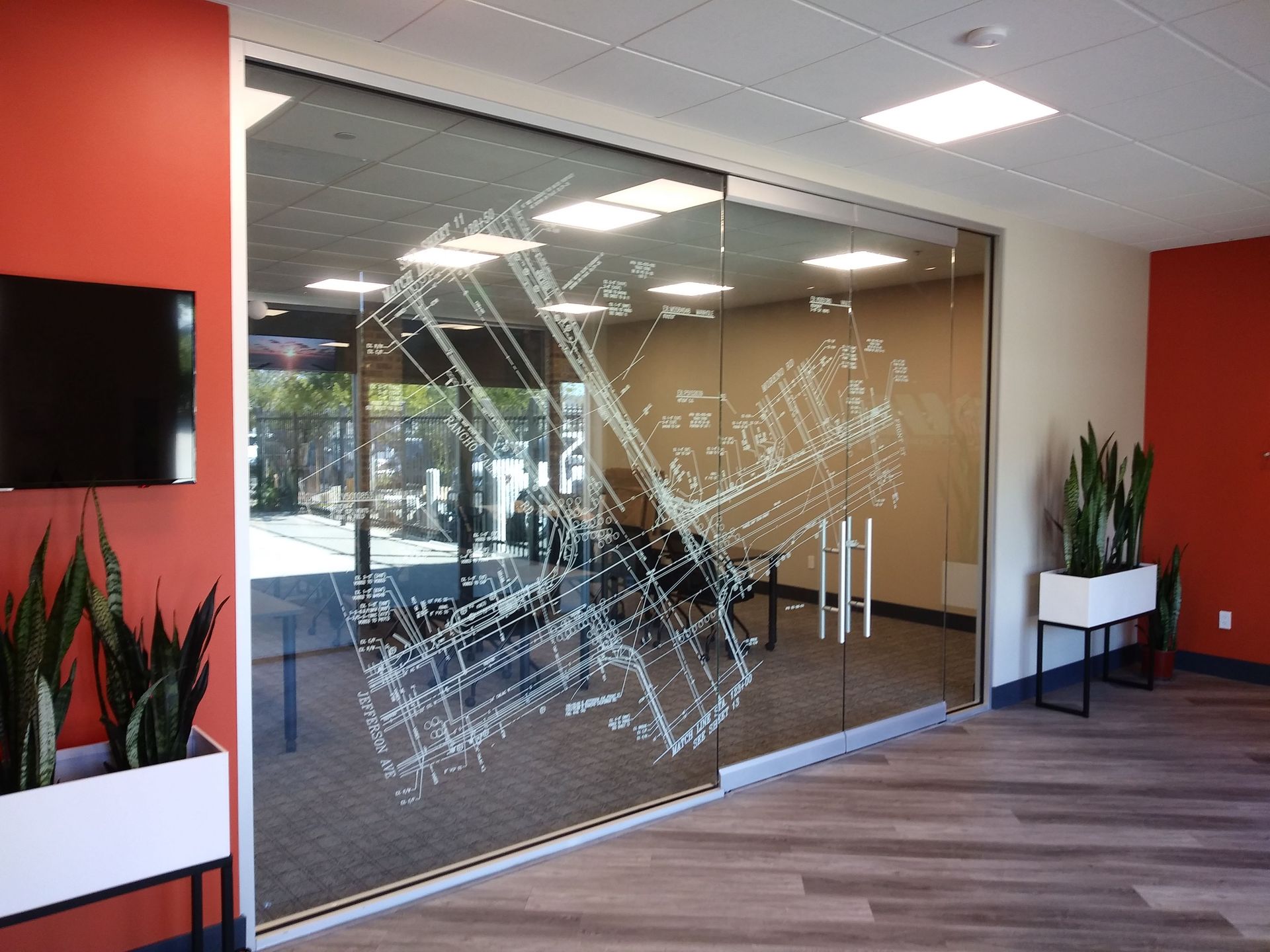 Modern office lobby with glass walls, red accent walls, wall-mounted TV, and potted plants