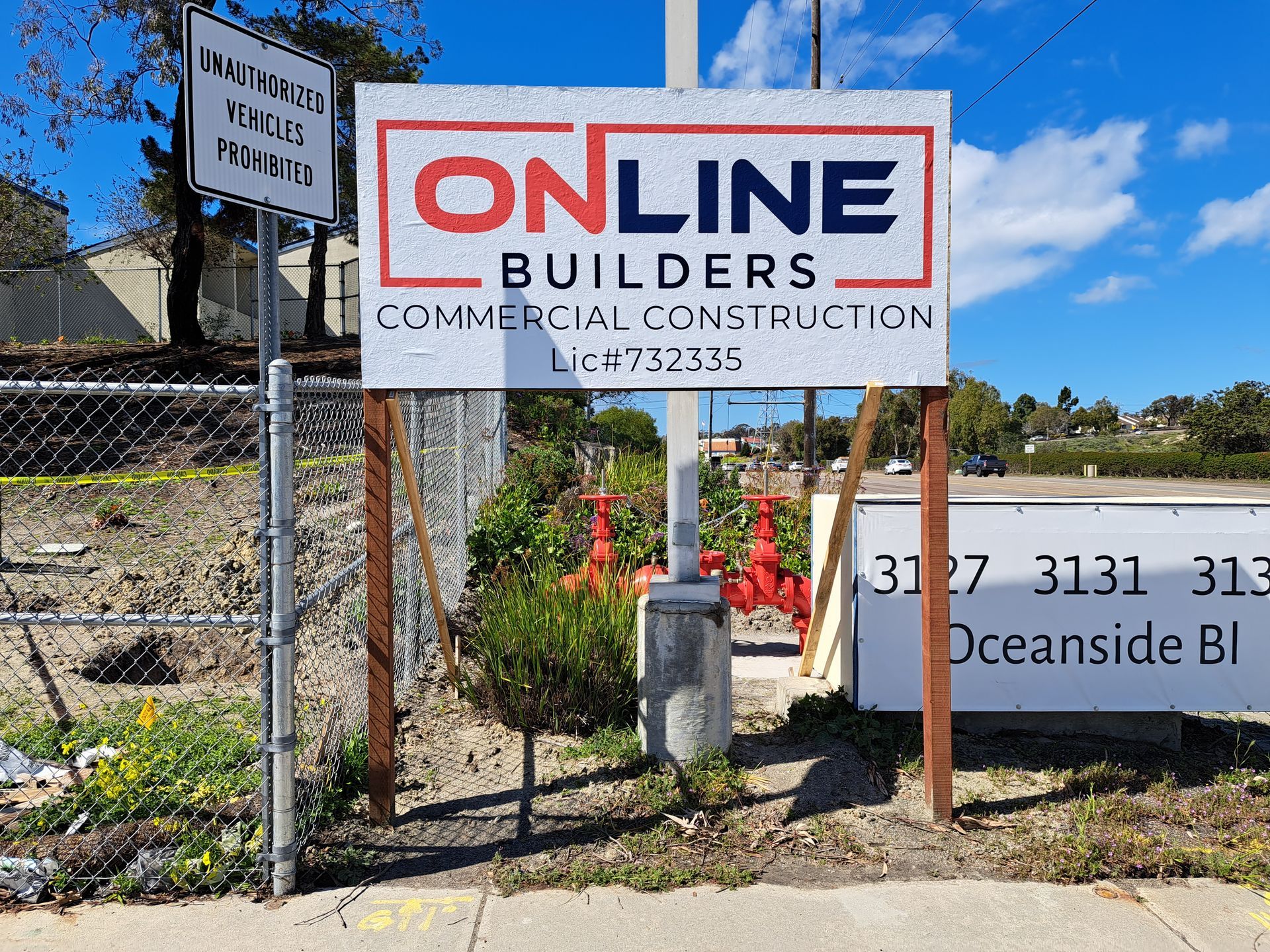 Construction signs for ONLINE Builders with an Oceanside Blvd address beside a road and hillside