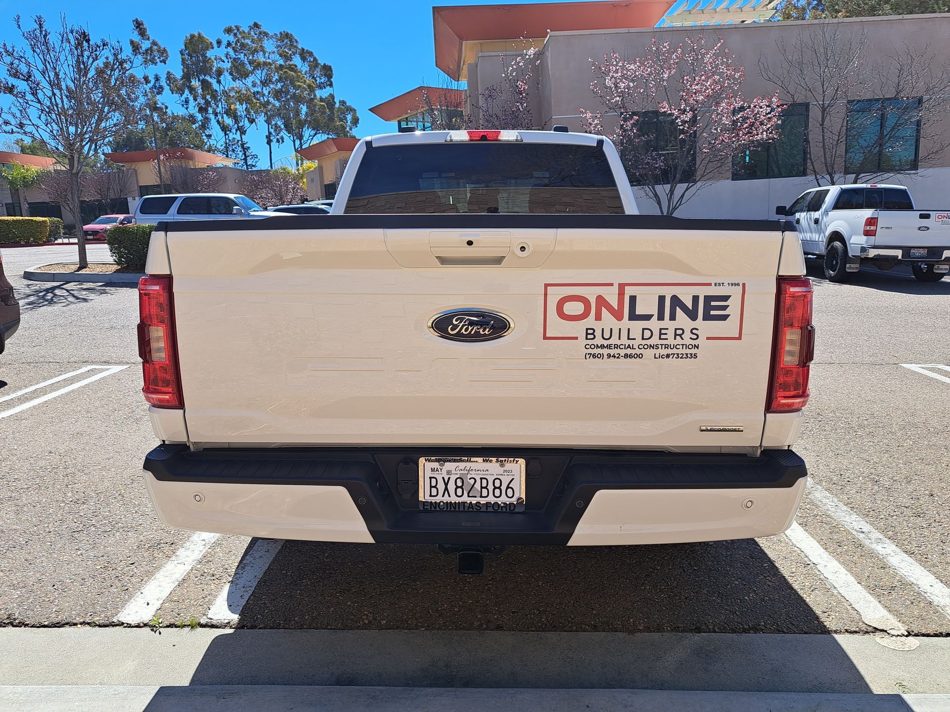 Beige Ford pickup truck with “ONLINE BUILDERS” logo parked in a sunny lot, rear view