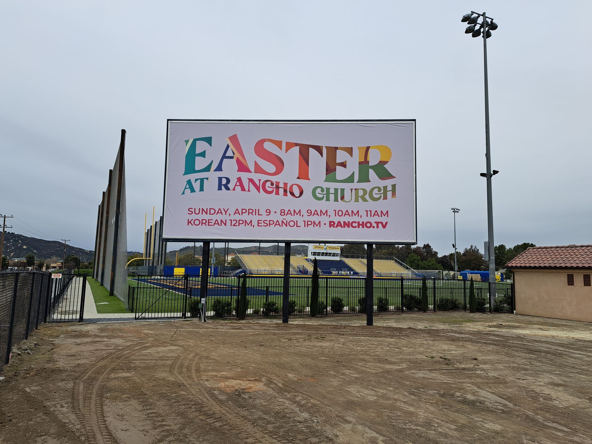 Sign for Easter at Rancho Church beside a dirt lot and fenced entrance